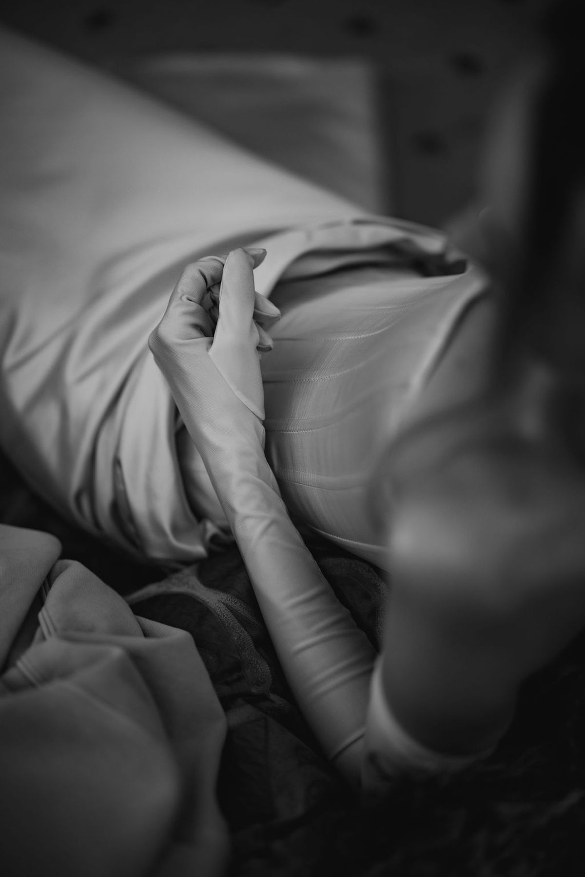 A gloved hand rests on white hospital bedding in a black and white medical photograph.