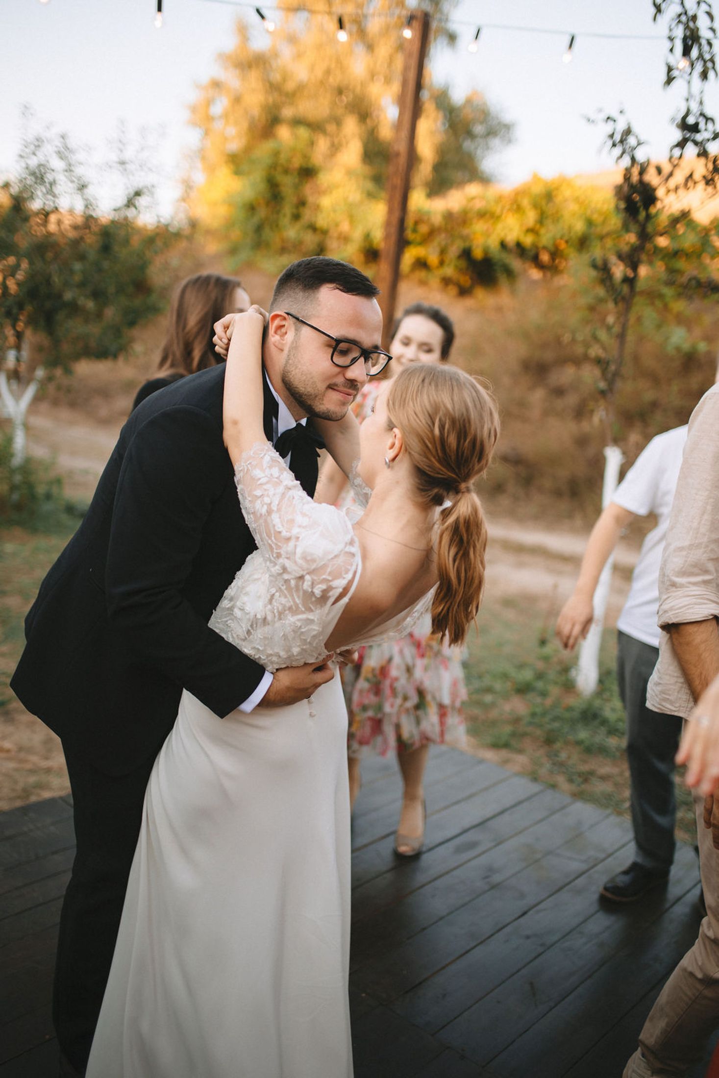 Romantic couple shares a dip kiss on wooden deck during sunset wedding celebration.
