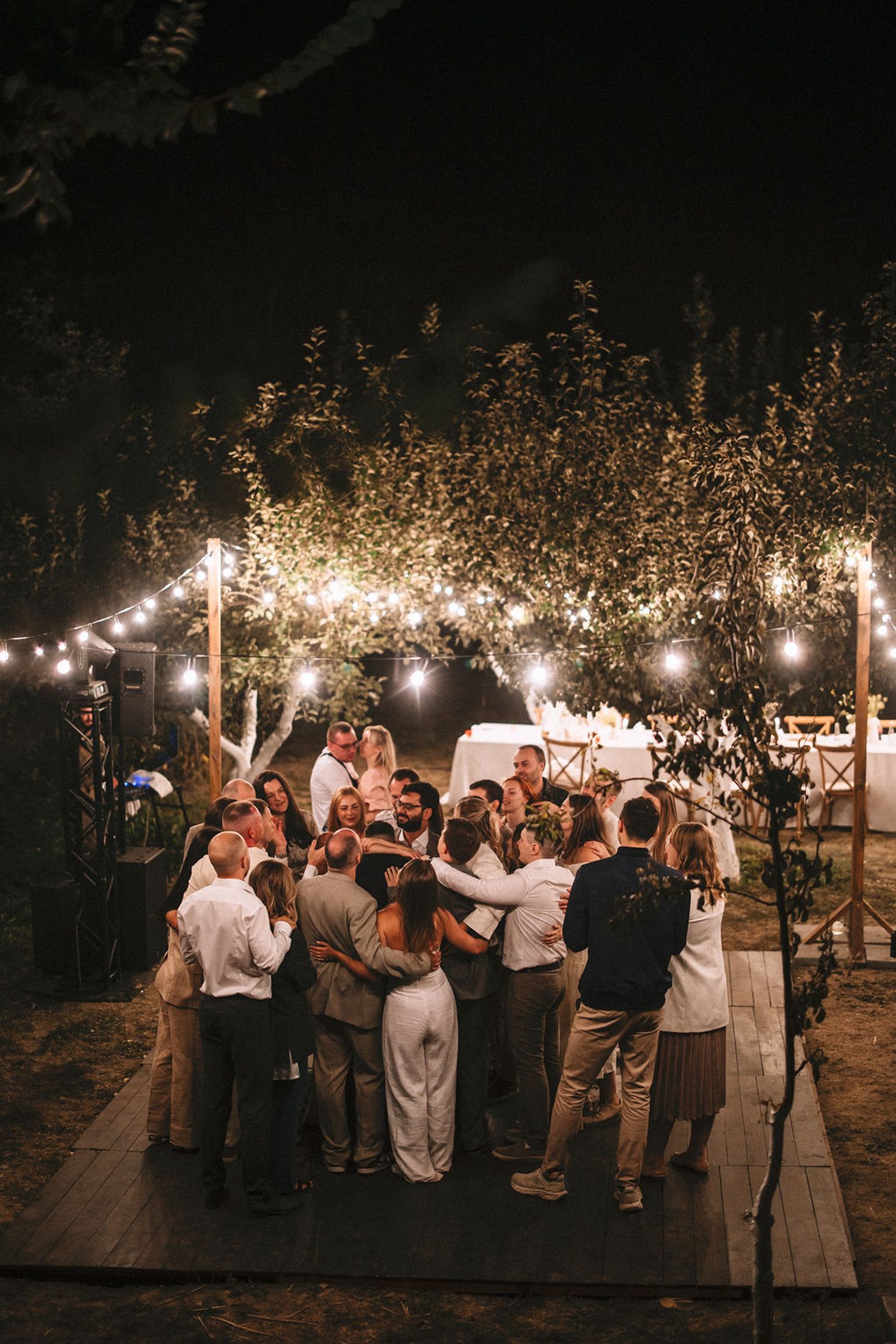 Wedding guests dance and celebrate under string lights at an outdoor evening reception.