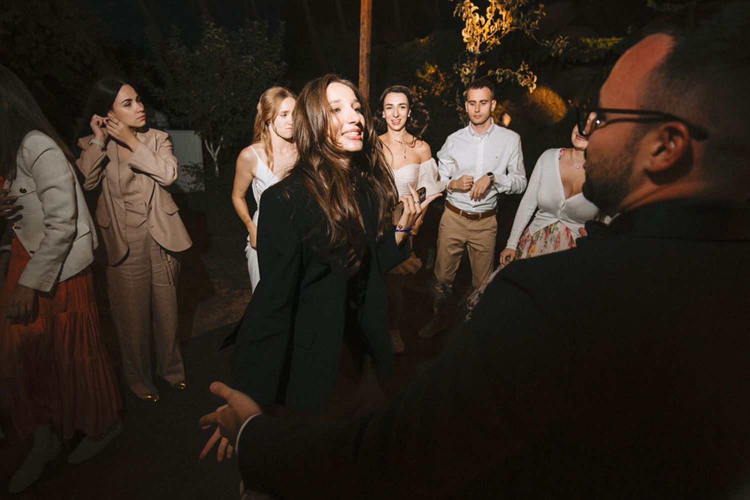 Wedding guests dancing and celebrating together at a dimly lit evening reception.