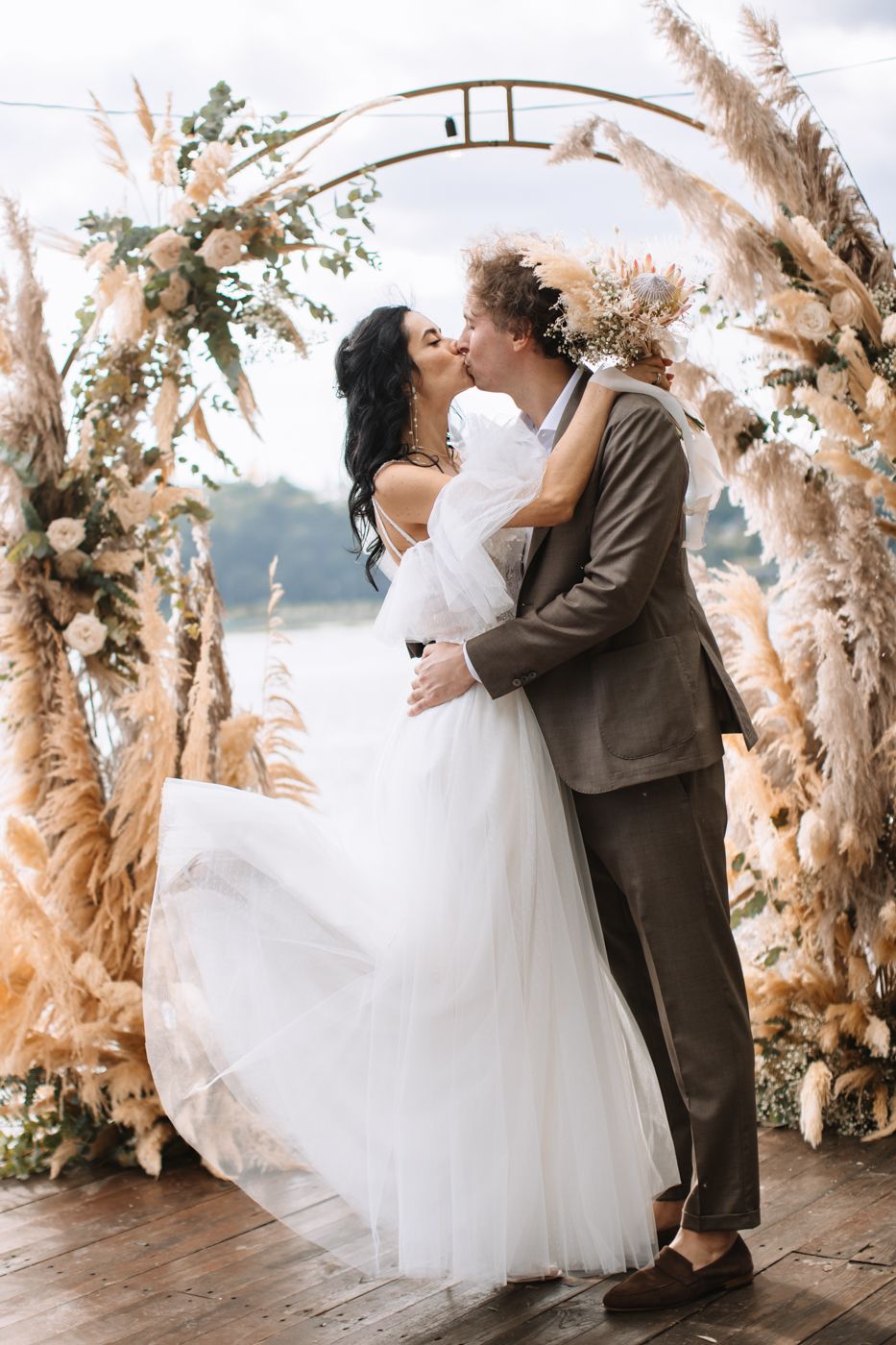 Romantic wedding couple dances surrounded by dried pampas grass and floral arrangements in an outdoor setting.