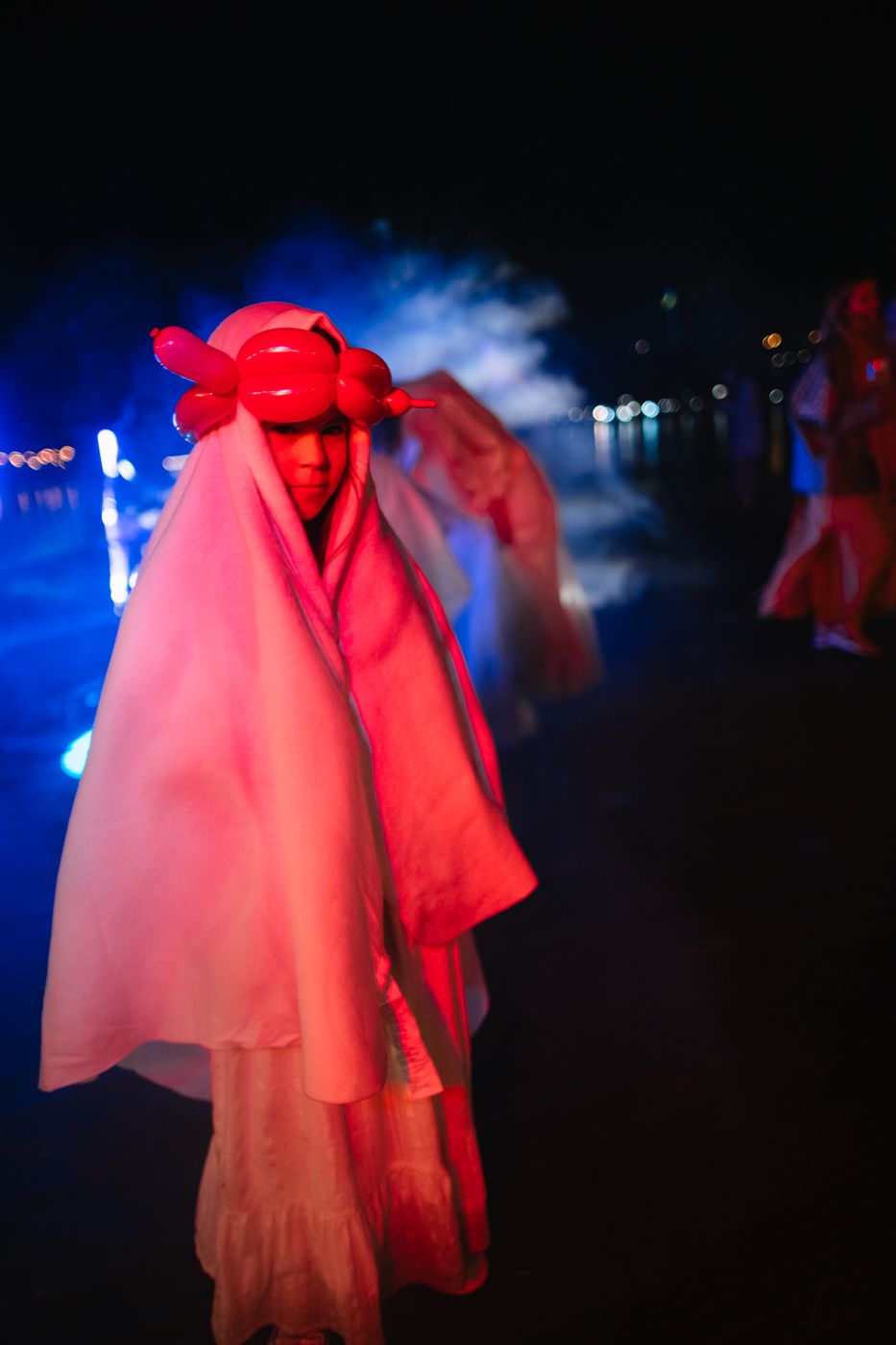 Ghostly figures in red-lit costumes perform a dramatic dance sequence on a dark stage.