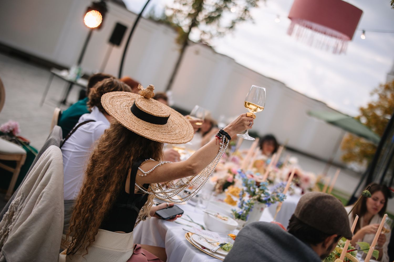People enjoying food and drinks at an outdoor social gathering with string lights and casual ambiance.