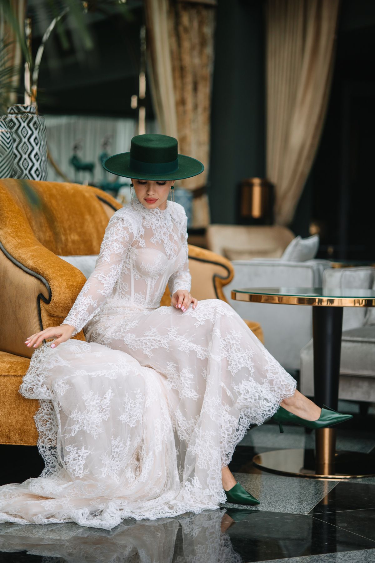 A figure in an elegant white lace dress and green hat reclines gracefully on a luxurious gold velvet sofa.