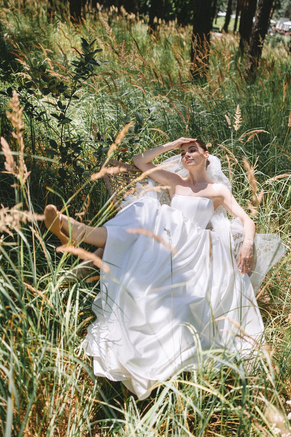 A person in a flowing white dress lies gracefully among tall grasses and wildflowers in a dreamy outdoor setting.