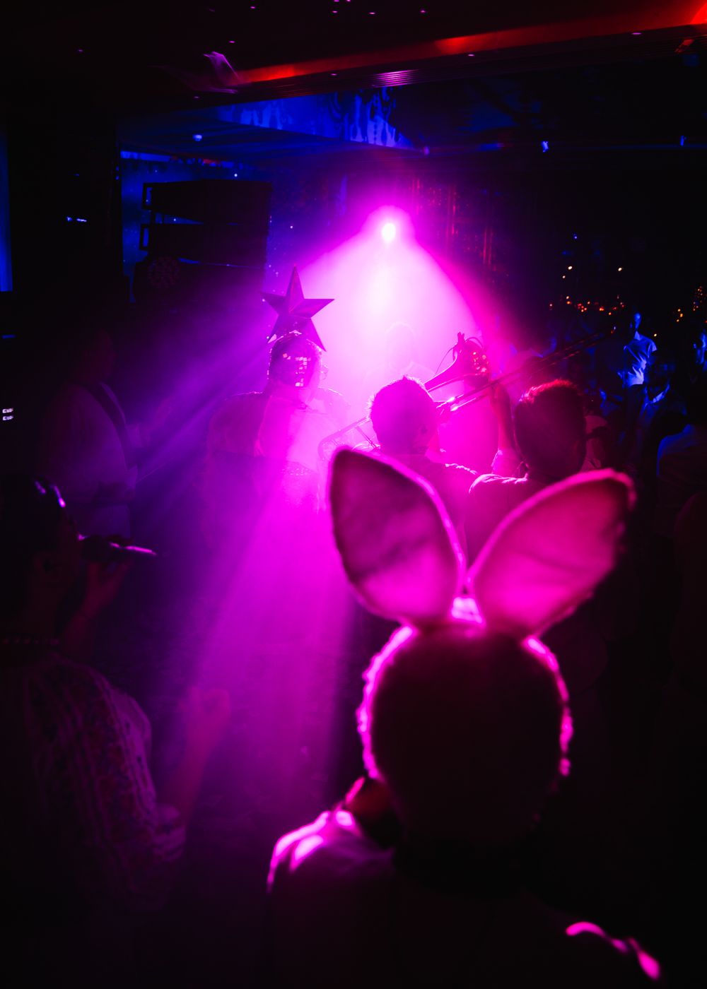 Silhouetted figures performing under intense magenta spotlights in a dark venue.
