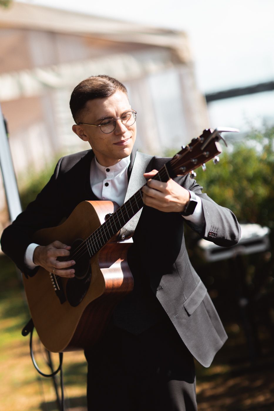 Classical guitarist in formal attire performs on acoustic guitar during outdoor event in natural lighting.