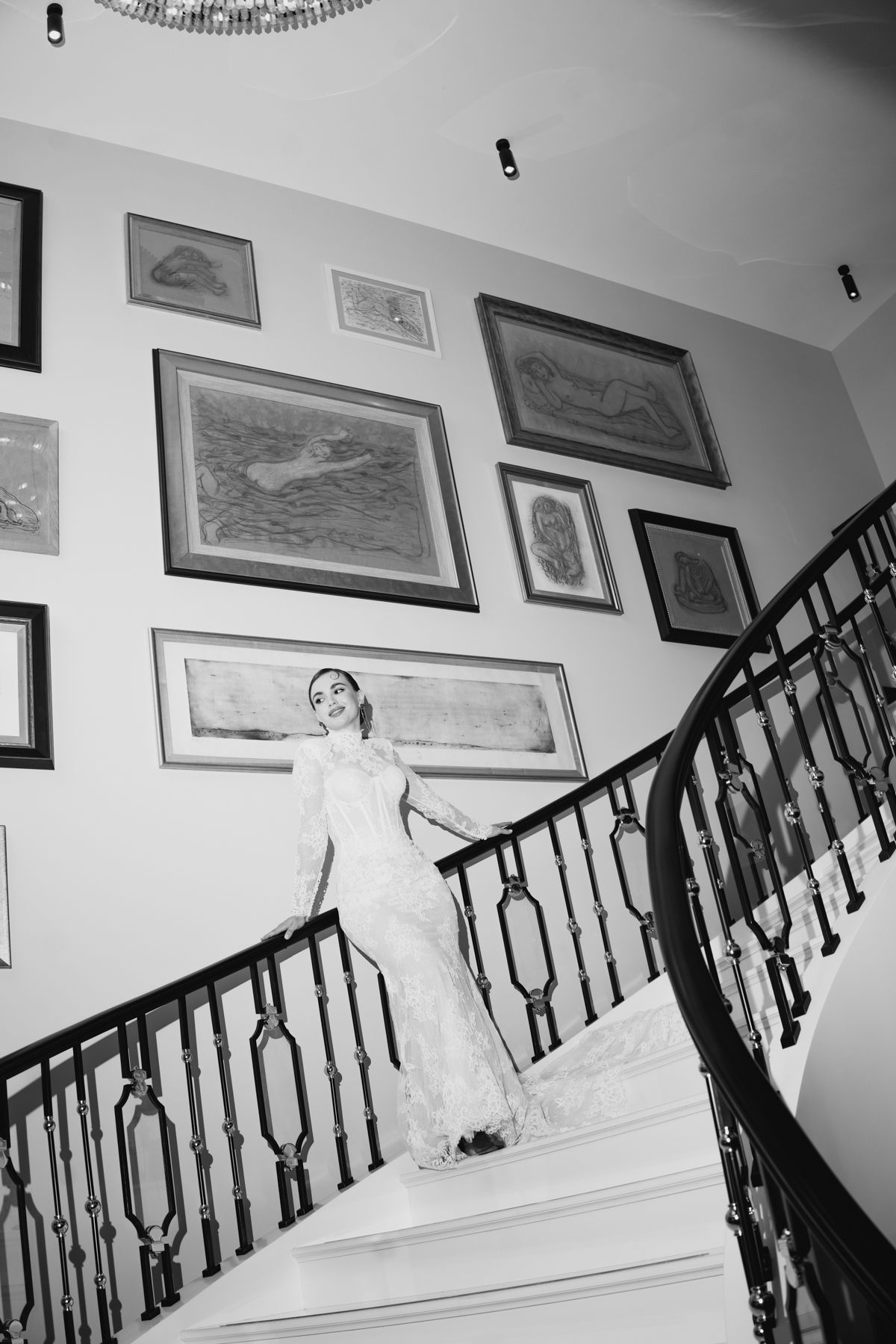 A black and white photograph shows an elegant staircase with ornate railings and framed artwork lining the white walls.