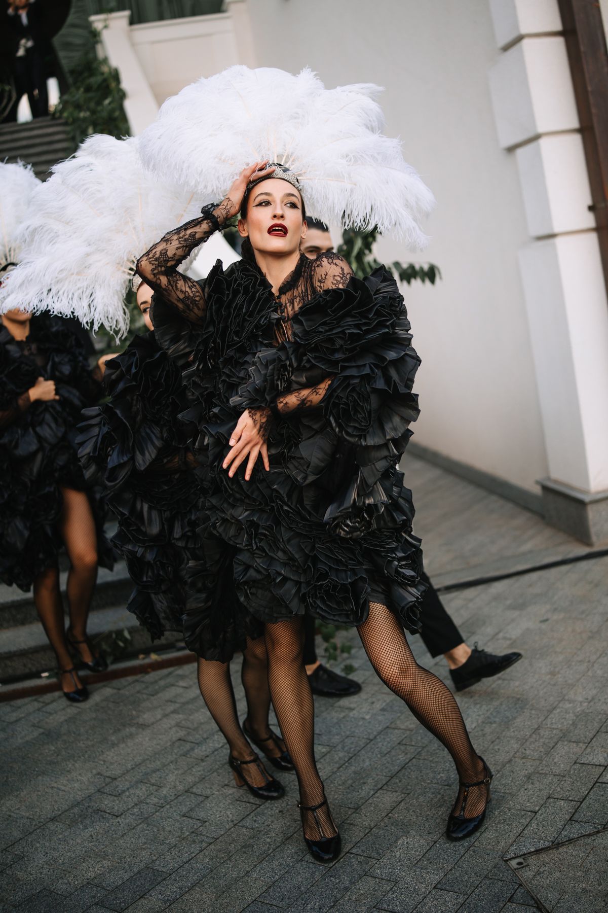 A person in a black ruffled dress and white feather boa poses playfully in a series of dynamic dance movements.