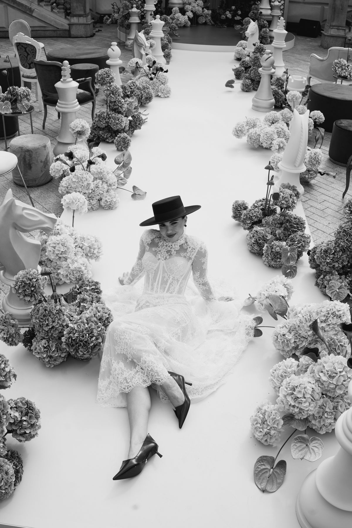 Black and white artistic photo sequence showing a person in white attire and hat sitting among hydrangea flowers.
