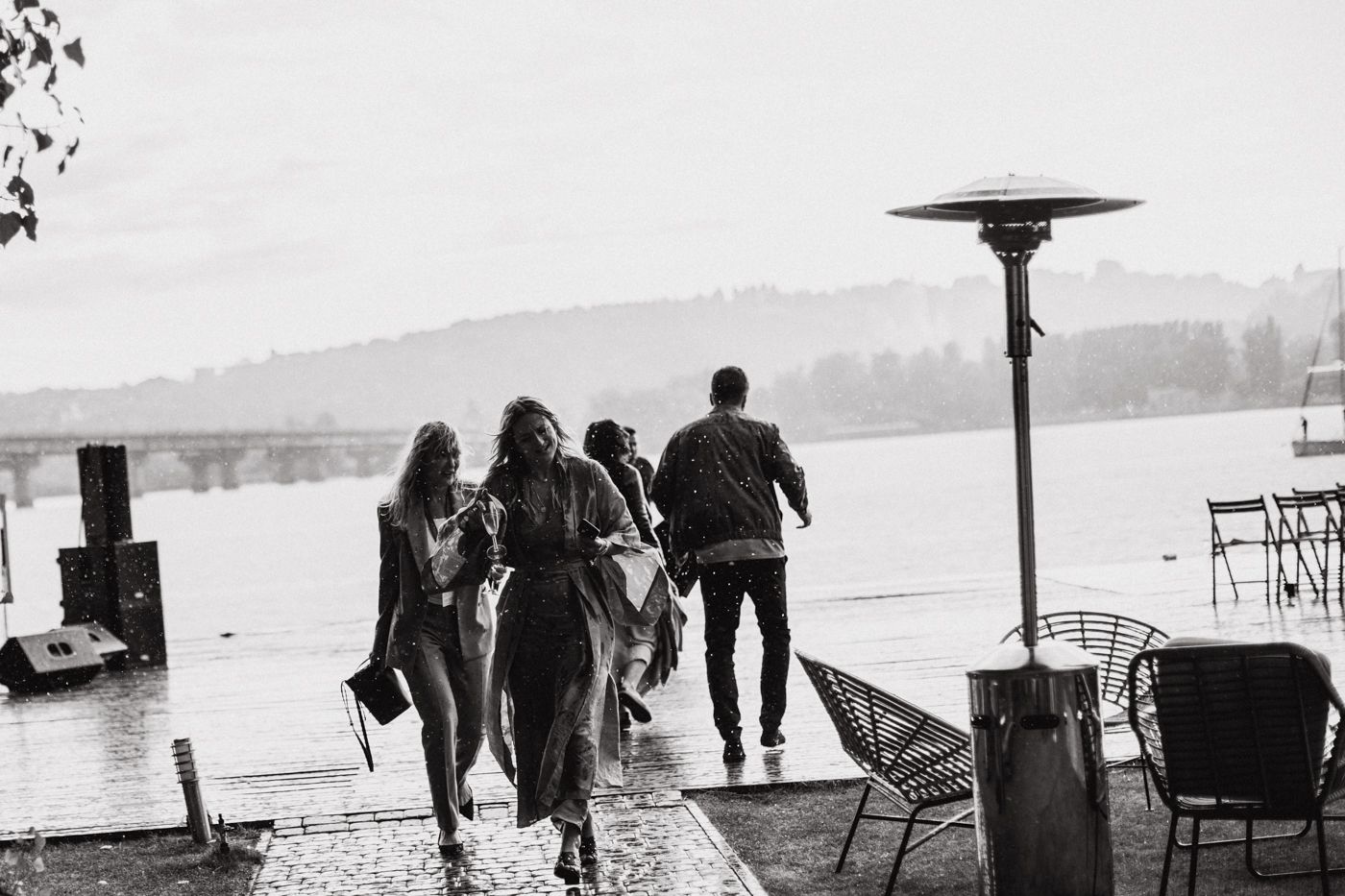 Black and white silhouettes of people walking along a waterfront with boats in the background.