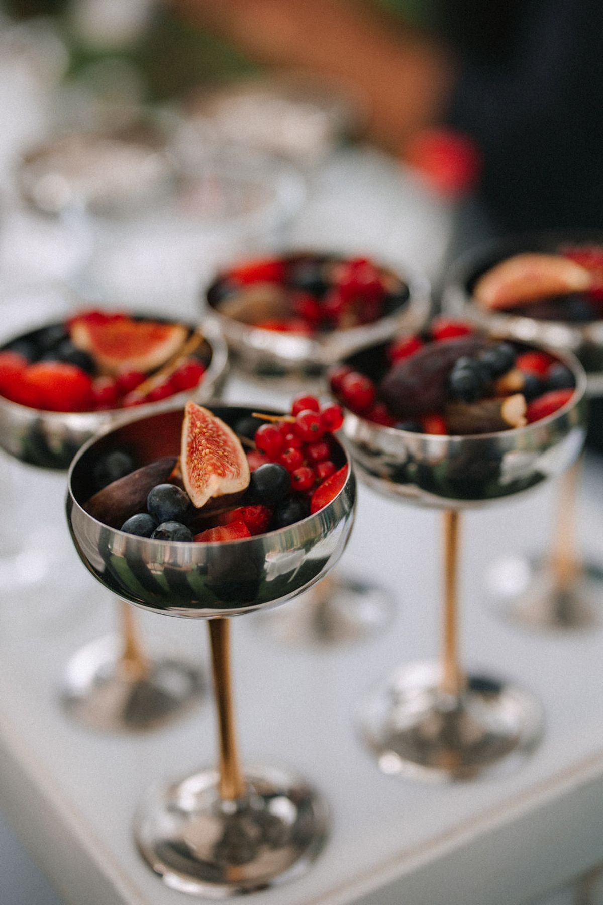 Elegant dessert coupe glasses filled with fresh berries and figs arranged in a stylish display on a white surface.