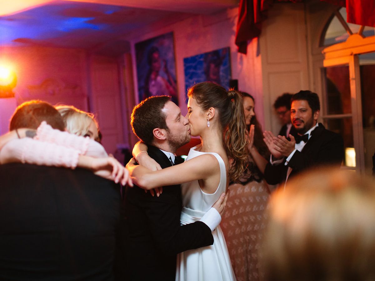 Newlyweds share a romantic kiss on the dance floor during their wedding reception under warm lighting.