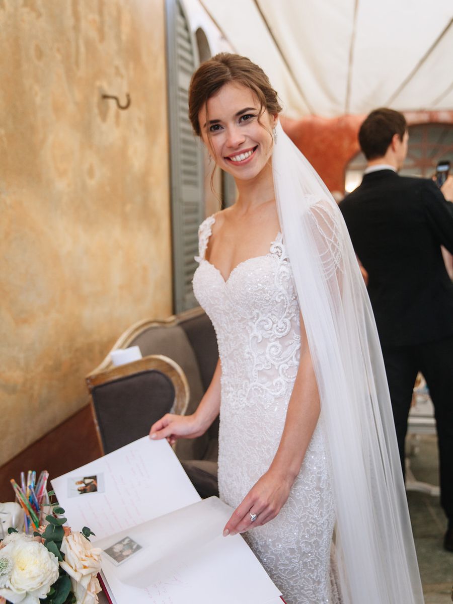 A bride in a white lace wedding dress signs documents during her wedding ceremony.