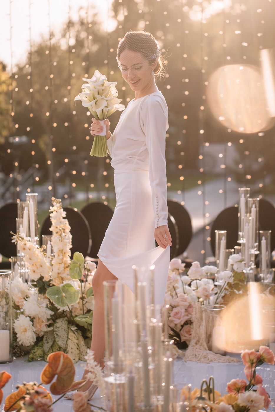 Elegant wedding reception table with white floral centerpieces and glowing candles at sunset.