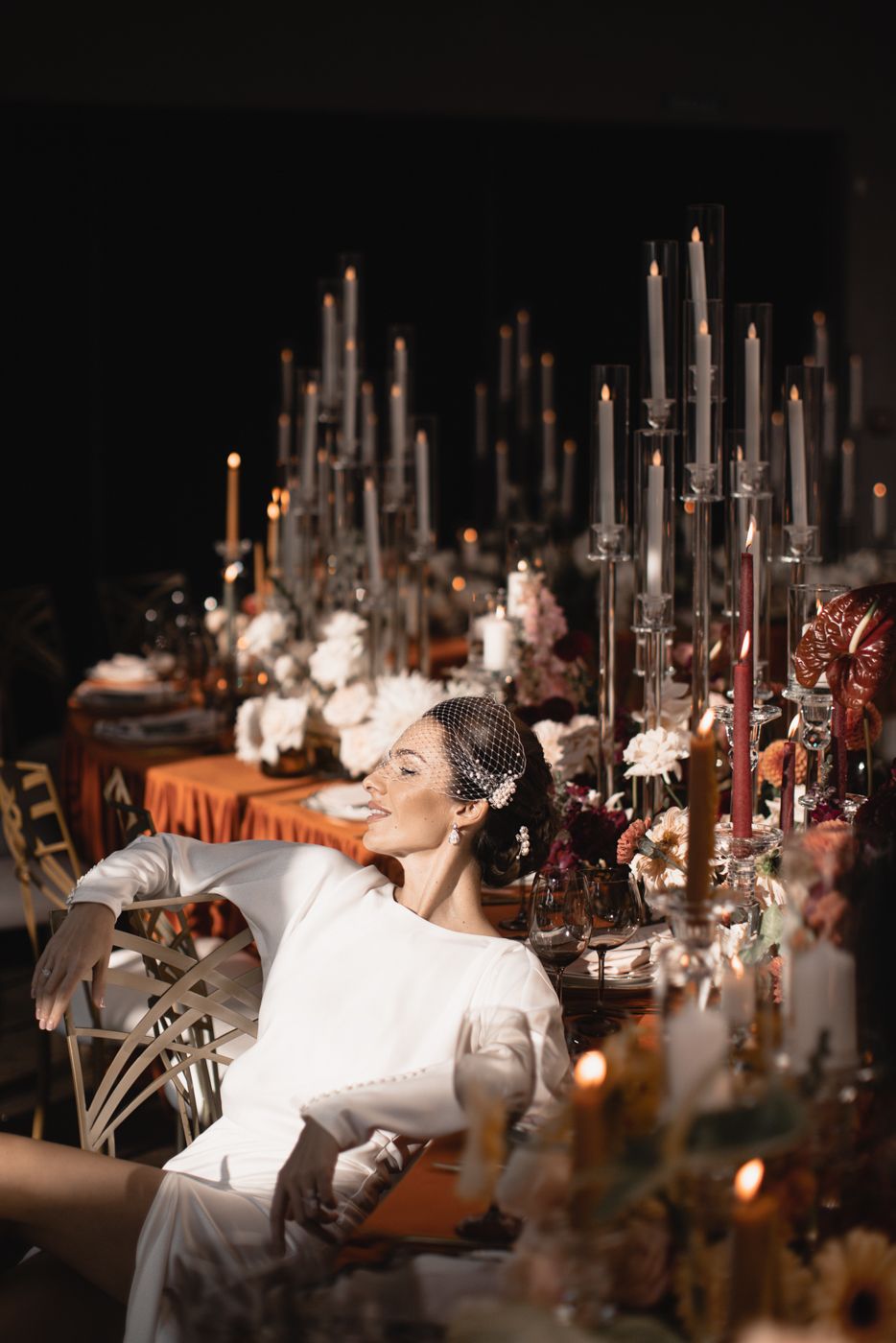 Elegant wedding reception table decorated with tall candles and floral arrangements in warm ambient lighting.