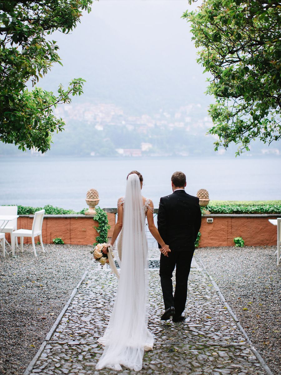 Wedding couple walks along scenic stone path overlooking Lake Como in Italy during intimate outdoor ceremony.