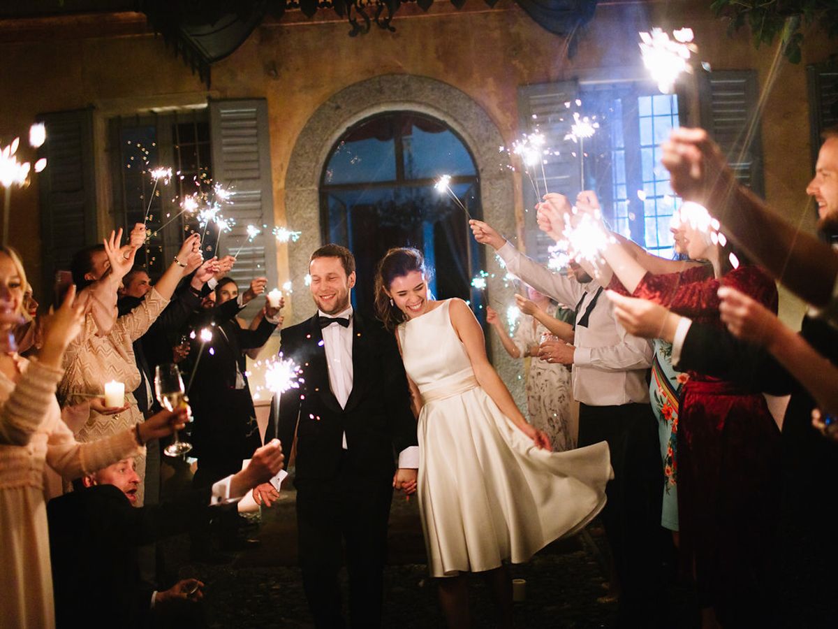 Wedding guests hold sparklers creating a glowing tunnel of light during an evening outdoor celebration.