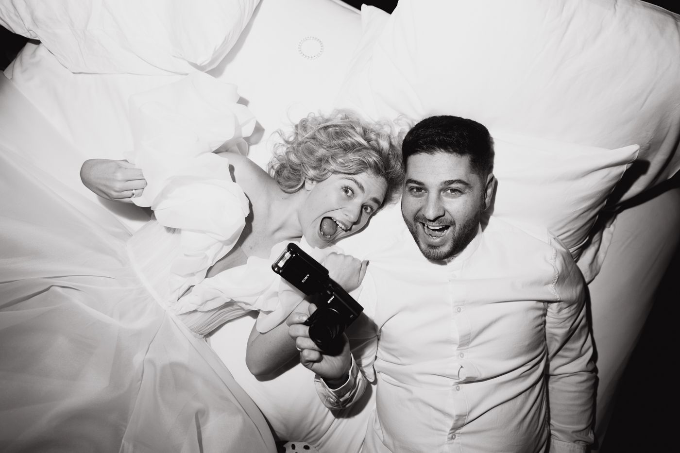 Playful black and white sequence of couple on white bedding.