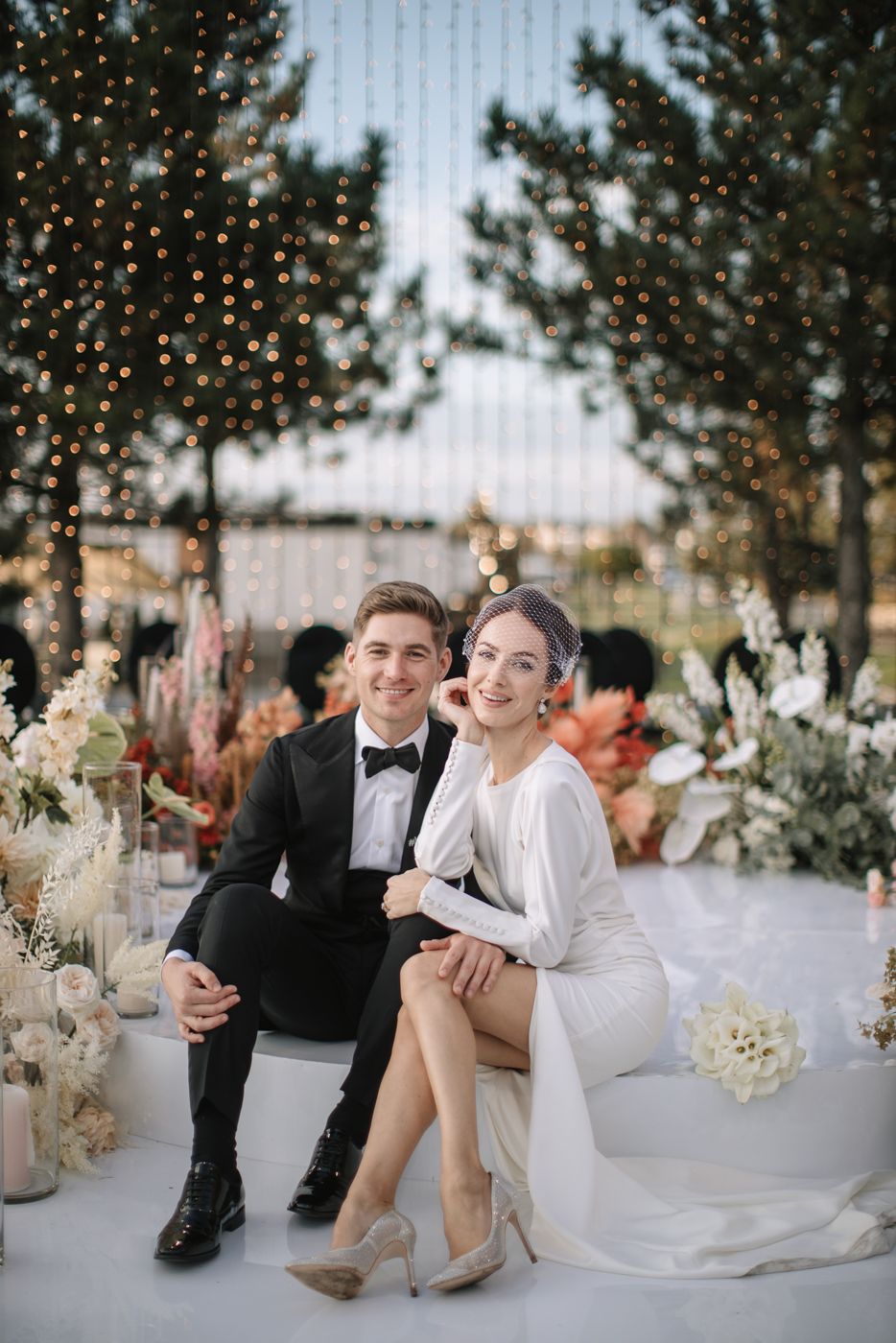 Elegant wedding reception setup with white decor and twinkling lights in an outdoor setting.