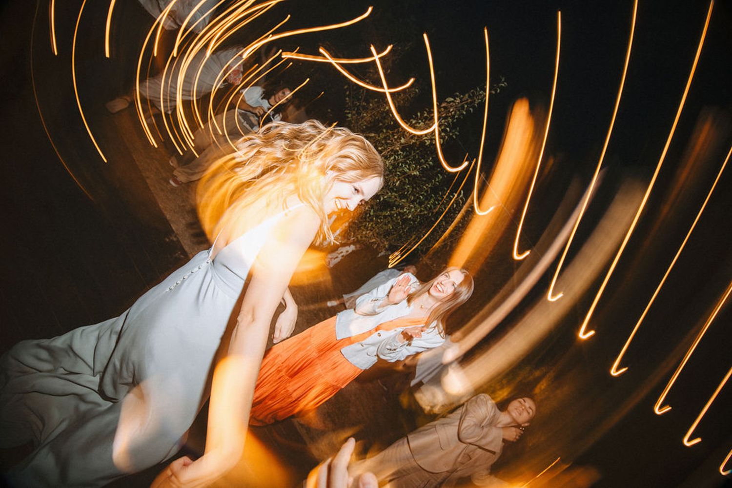 Long exposure photograph shows swirling orange light trails against a dark background creating an abstract pattern.