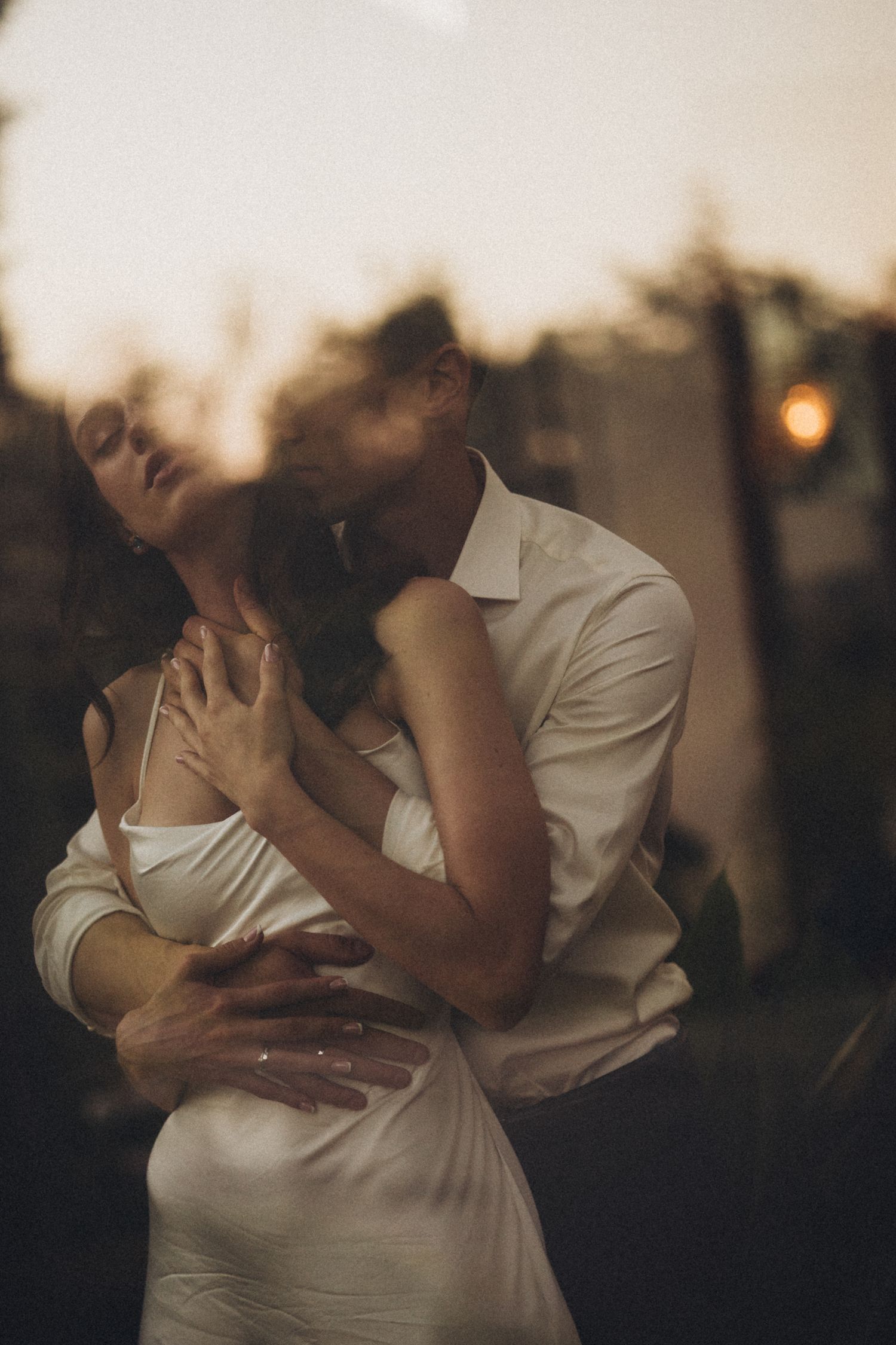 Soft focus photograph of two people in white attire sharing an intimate moment at dusk.