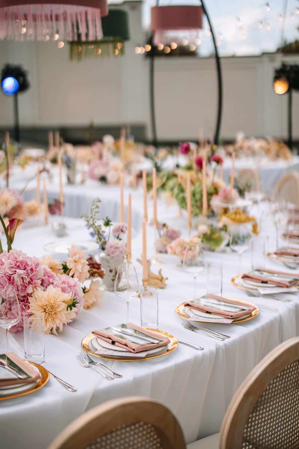 Elegant wedding reception table settings with white linens, gold charger plates, and pink floral centerpieces.
