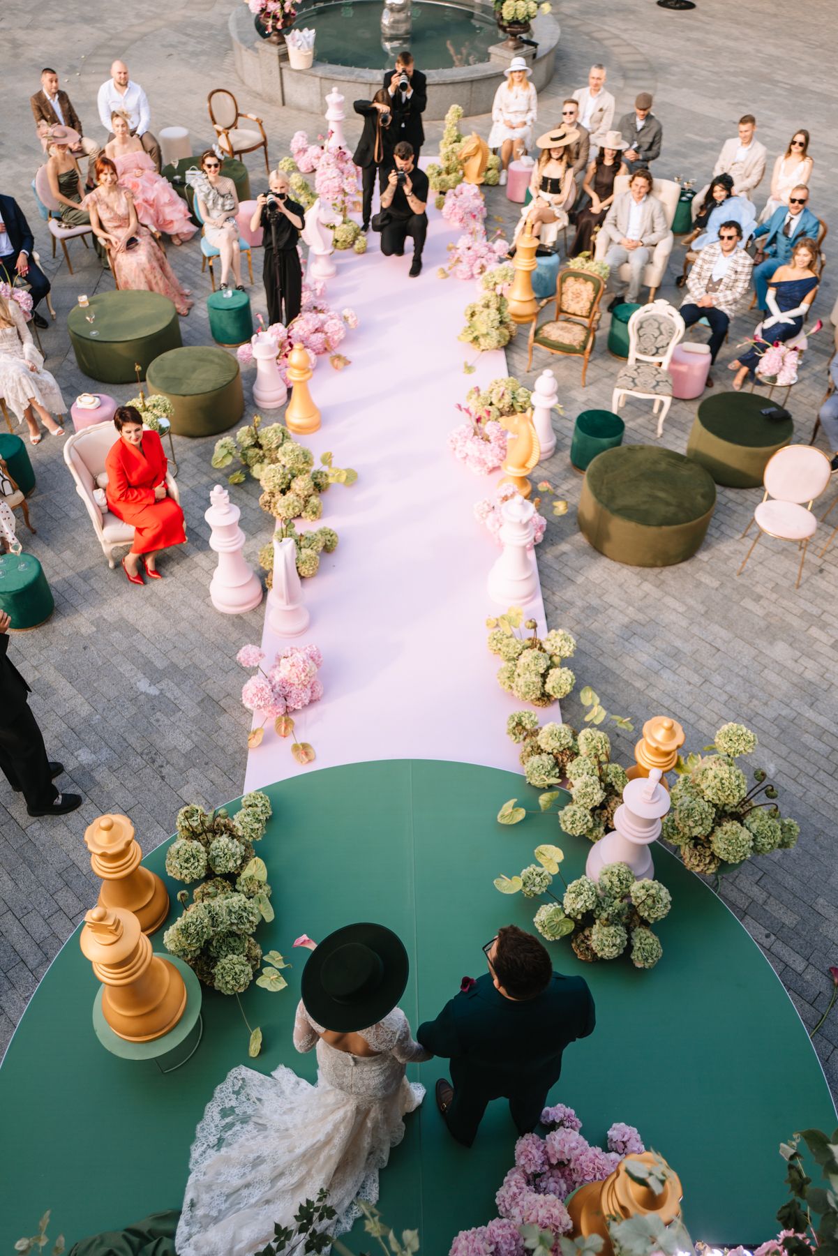 Aerial view of a wedding ceremony setup with a green circular carpet and floral arrangements on a stone patio.