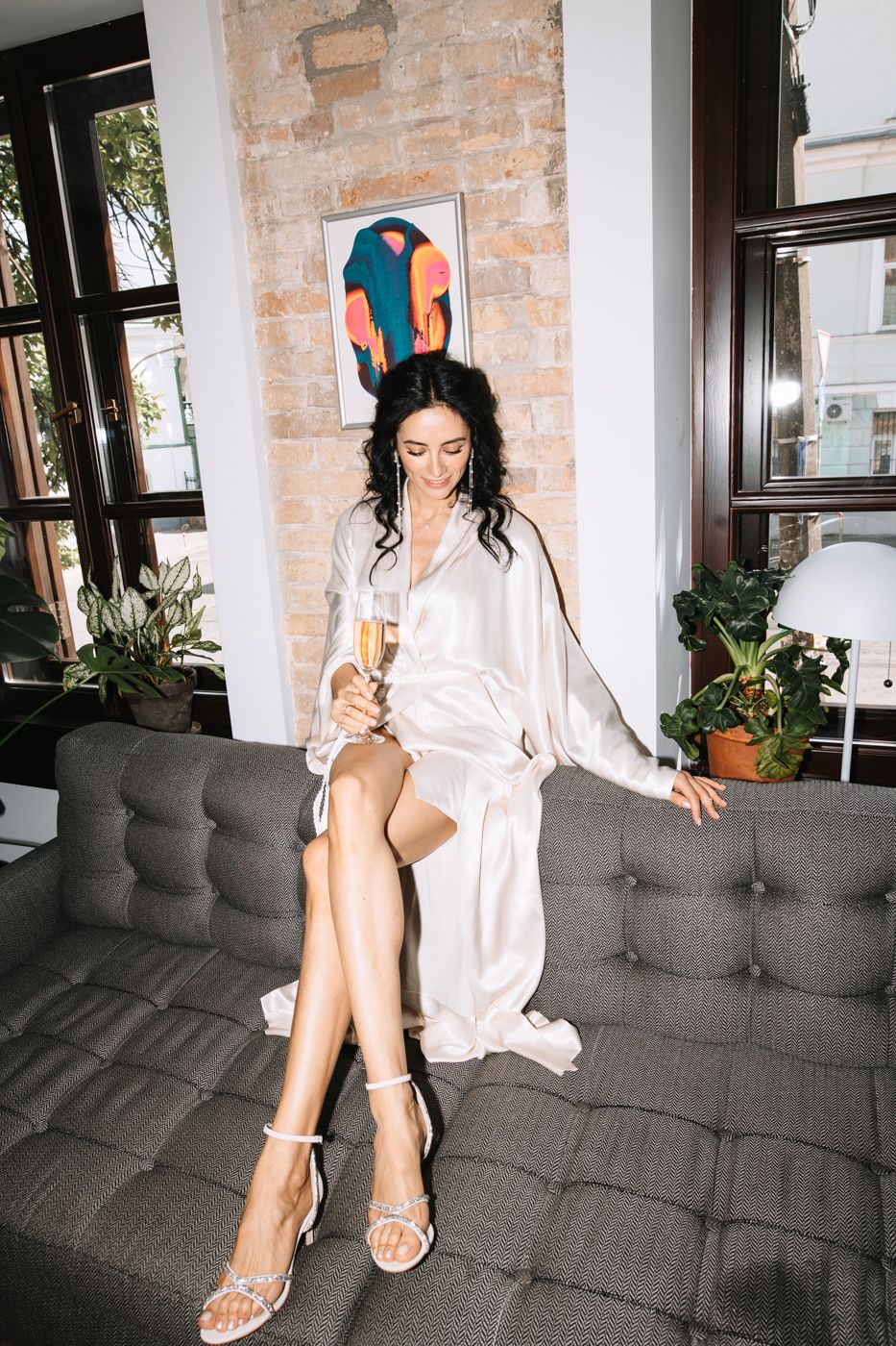 A person in a white button-down shirt relaxes on a gray tufted couch in a room with exposed brick walls.