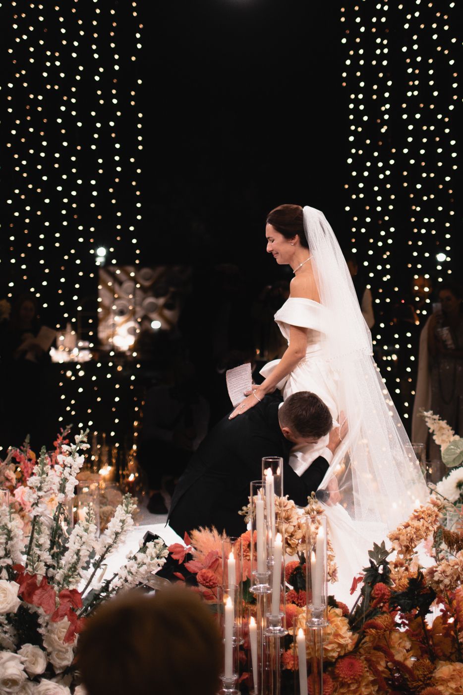 A wedding ceremony scene with cascading fairy lights and pink floral arrangements.