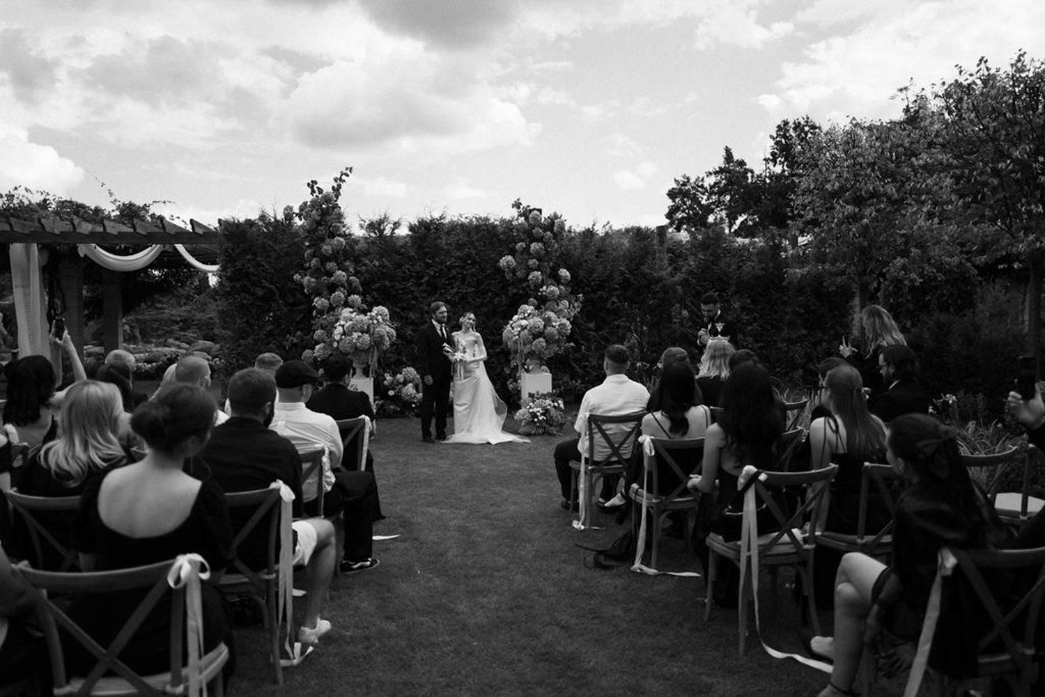 Black and white panoramic view of a crowd gathered outdoors at a community event with tents and people mingling.