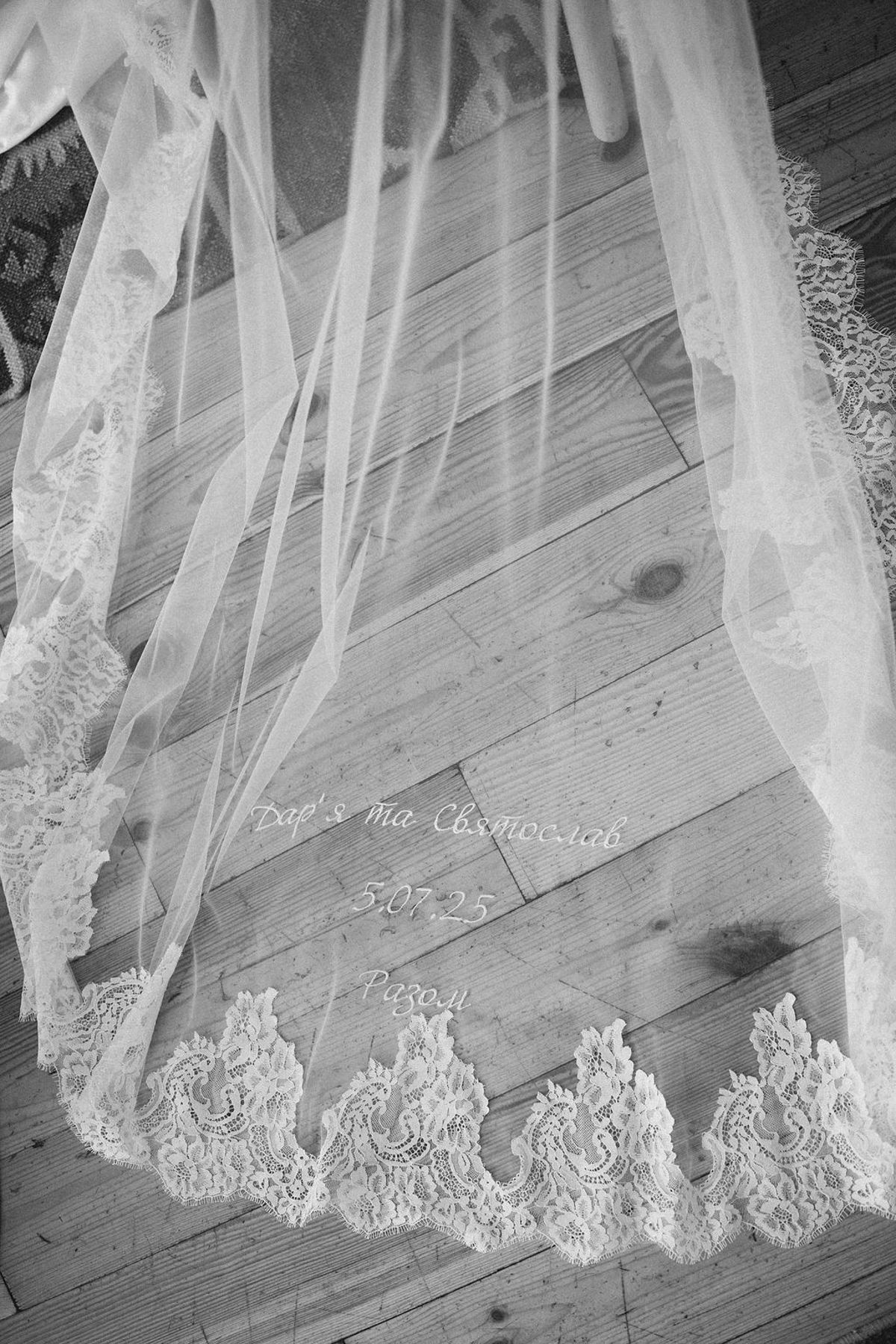 Close-up details of delicate white lace trim on a wedding dress hem against a light wooden floor.