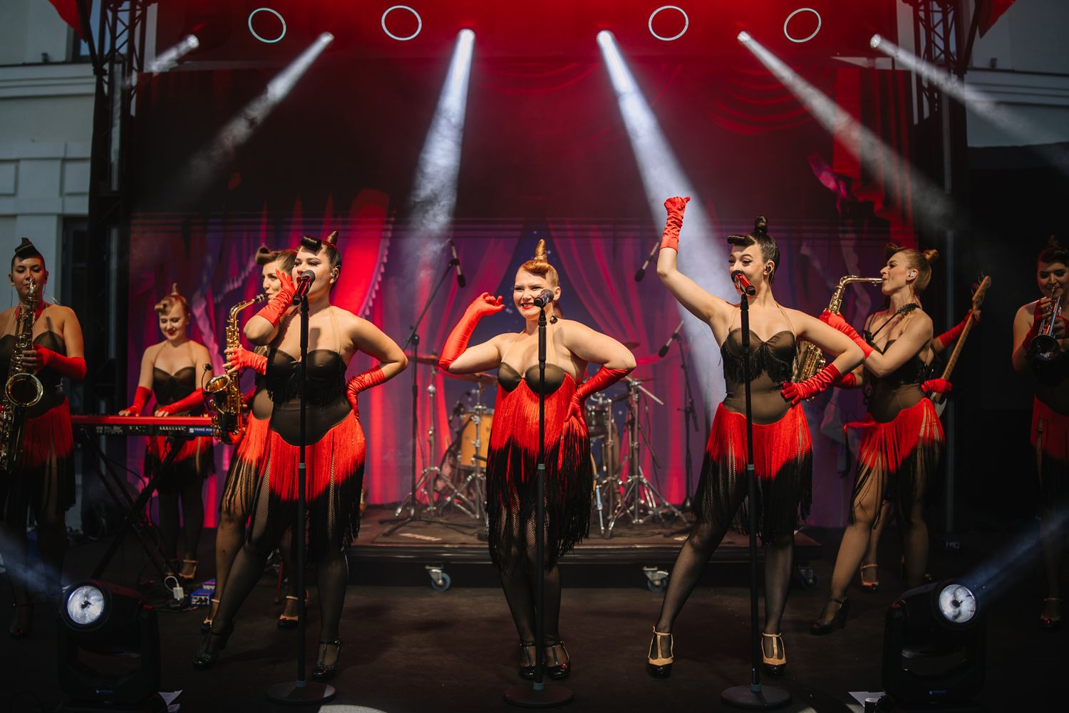 Dancers perform a high-energy cabaret show with red lighting and dramatic choreography on stage.