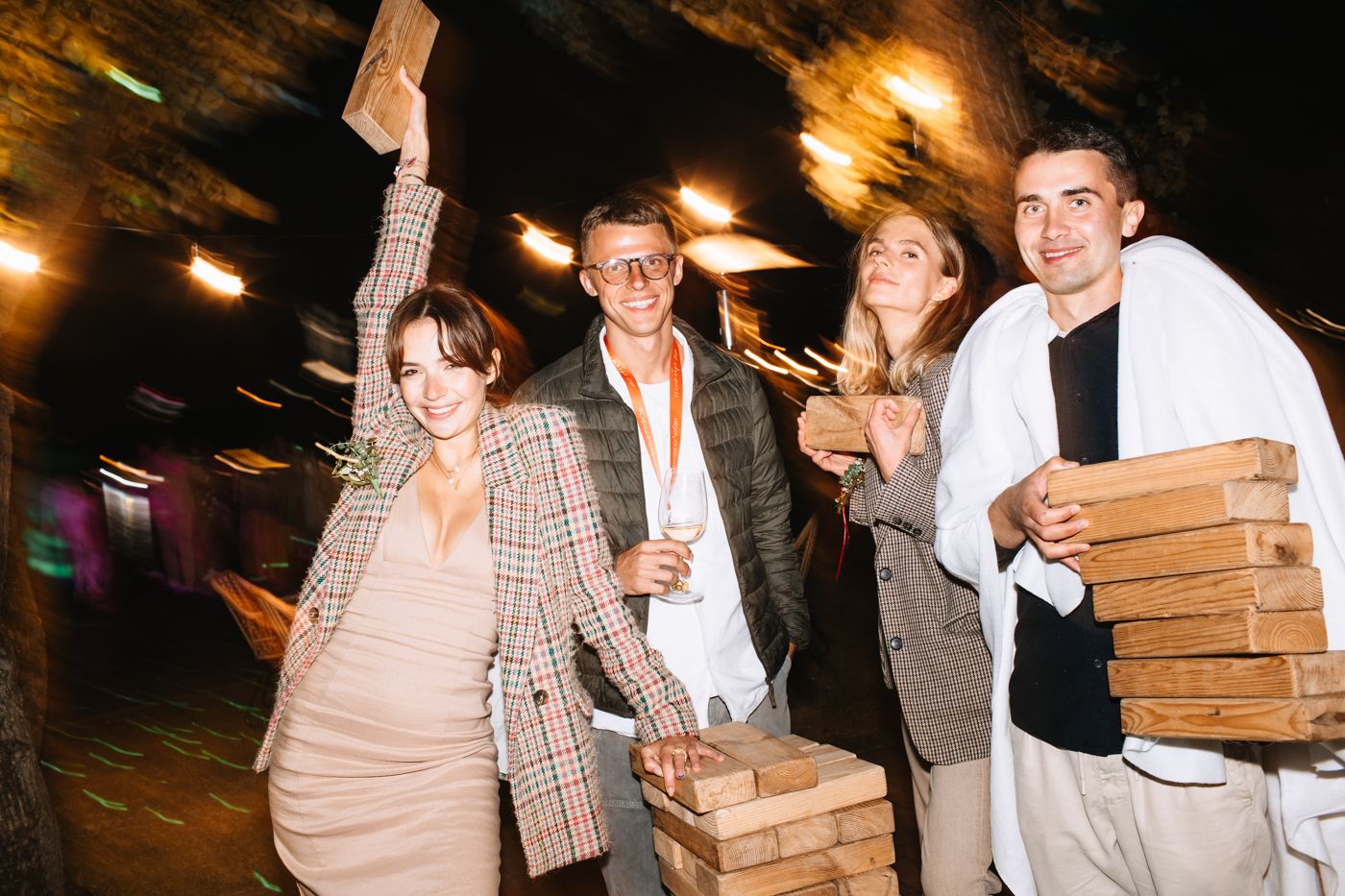 A group of friends celebrate at night while carrying stacks of pizza boxes and drinks outdoors.