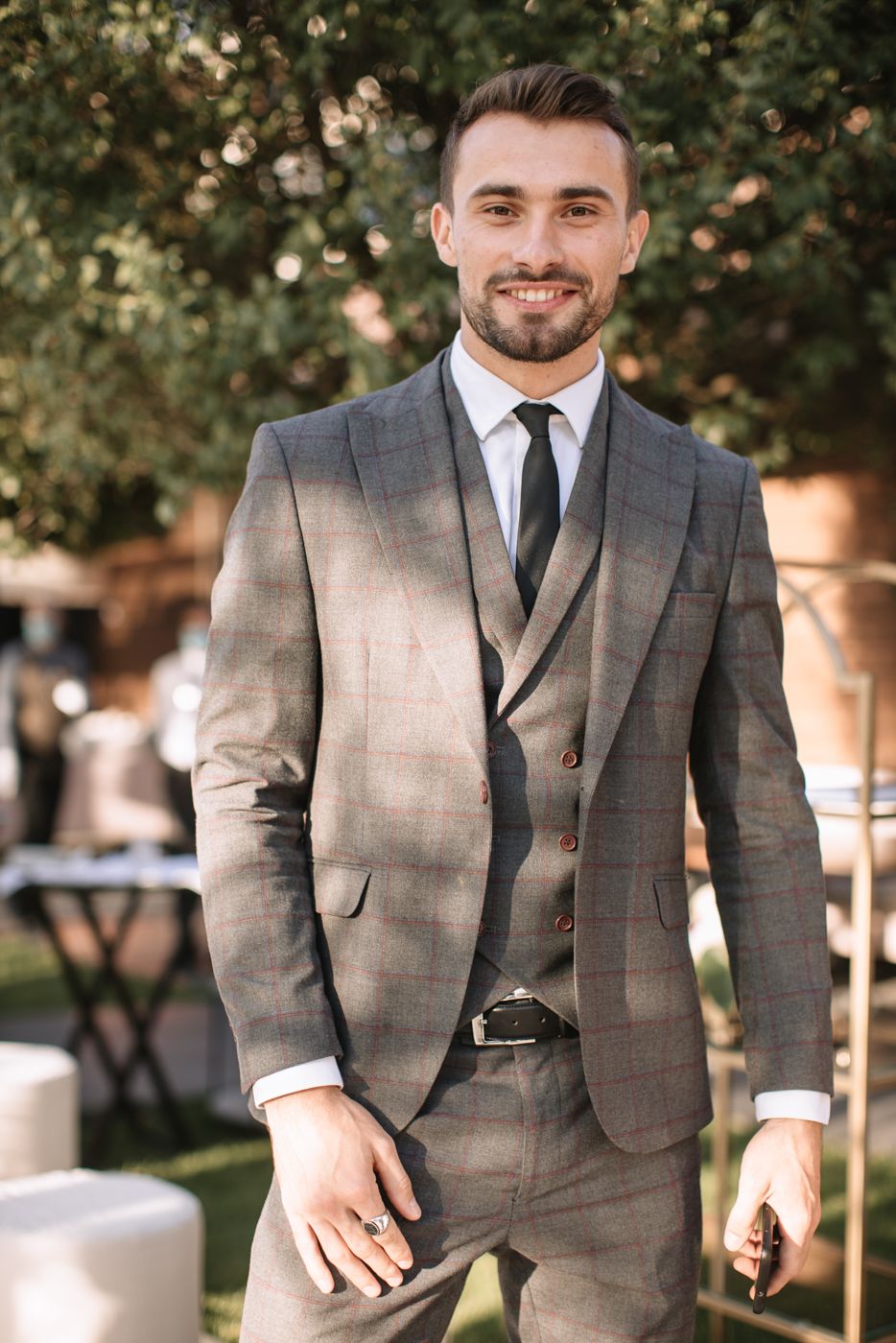 Formal portrait of person in grey plaid suit and tie at outdoor event.