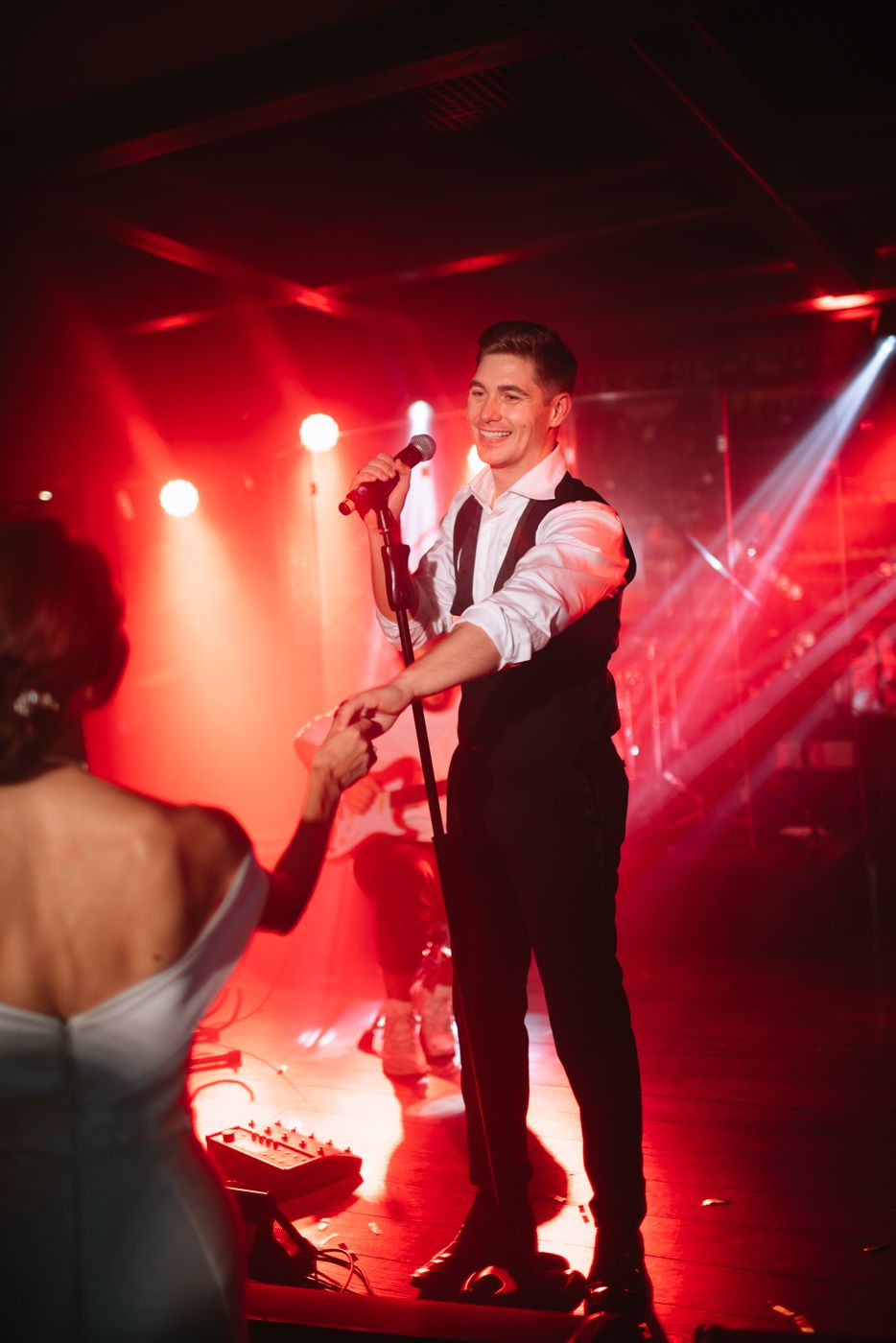 DJ performing at a wedding reception with dramatic red stage lighting.