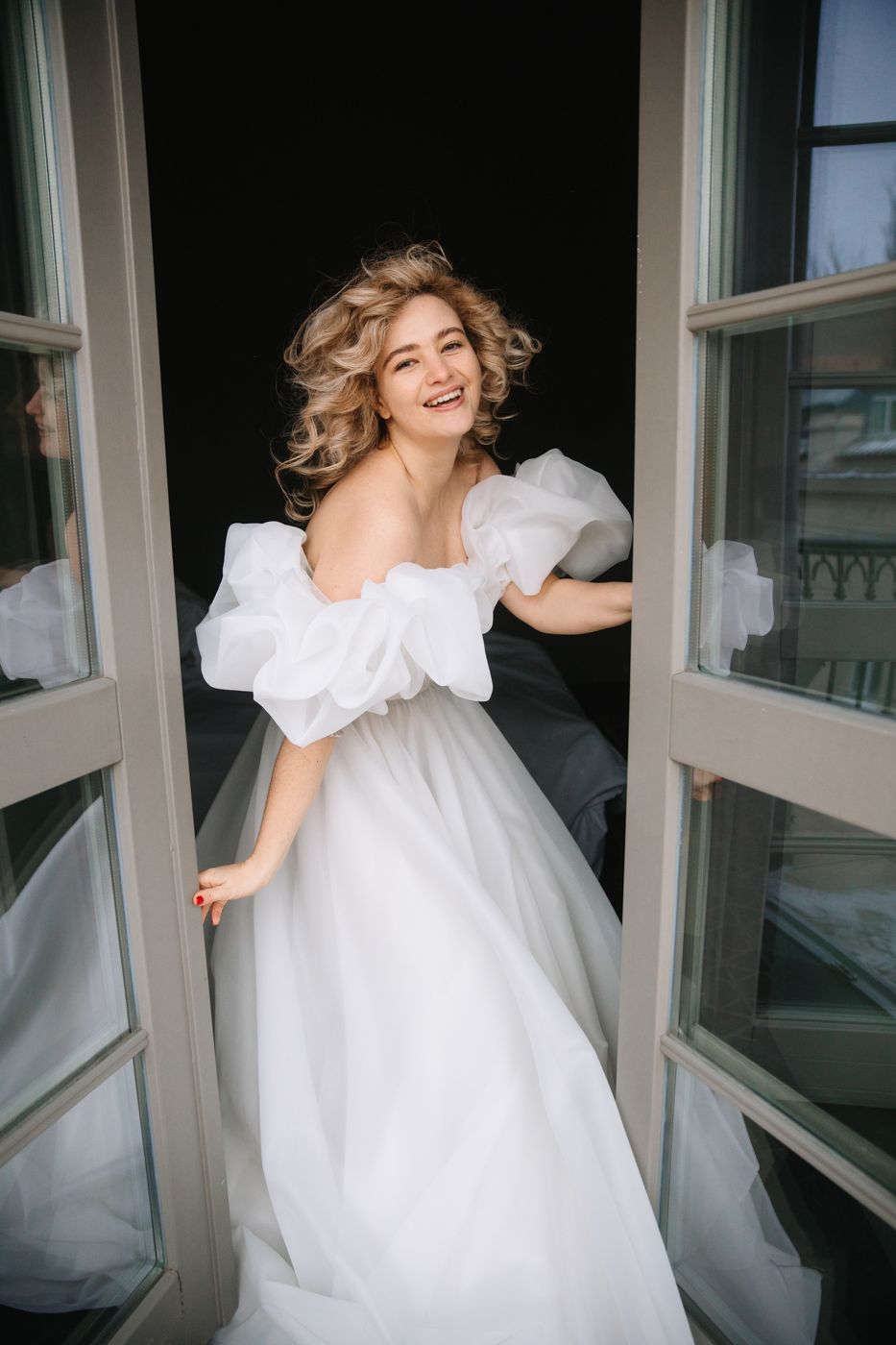 Person in white dress twirls joyfully by window in artistic photo series.