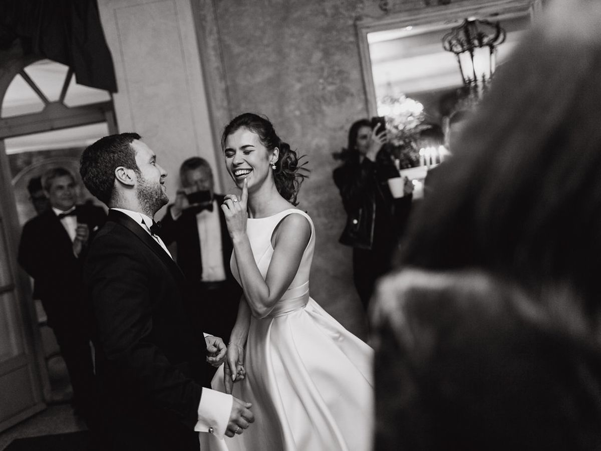 Wedding guests dancing and celebrating on a dimly lit dance floor at an indoor reception.
