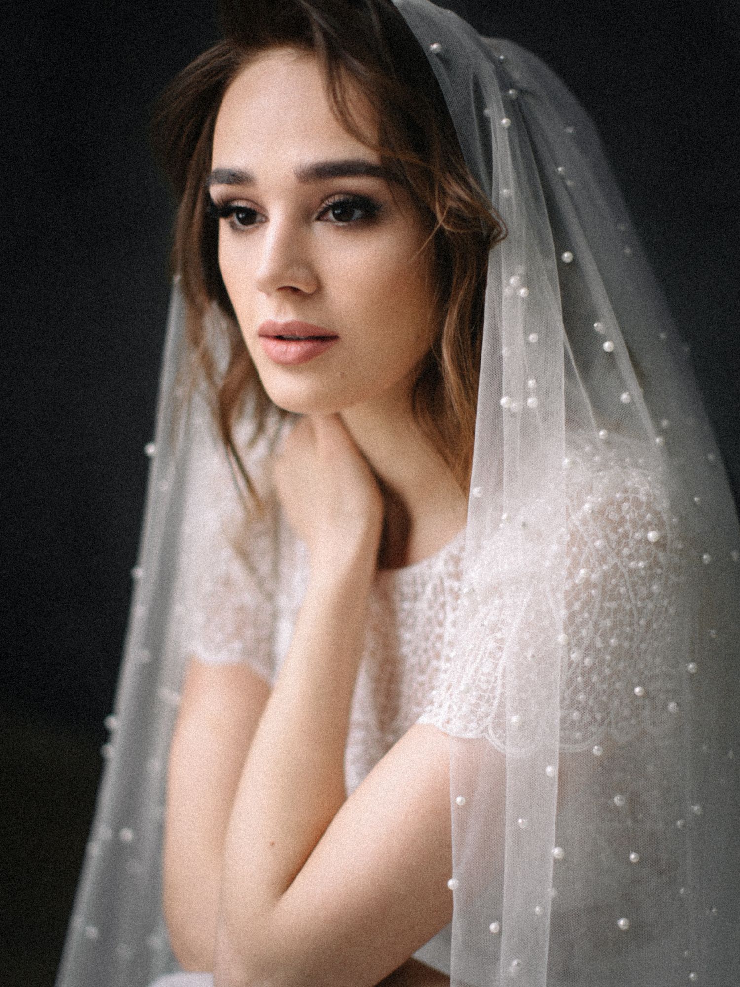 A bride in a delicate tulle veil with sparkly details poses against a dark background in a romantic portrait series.