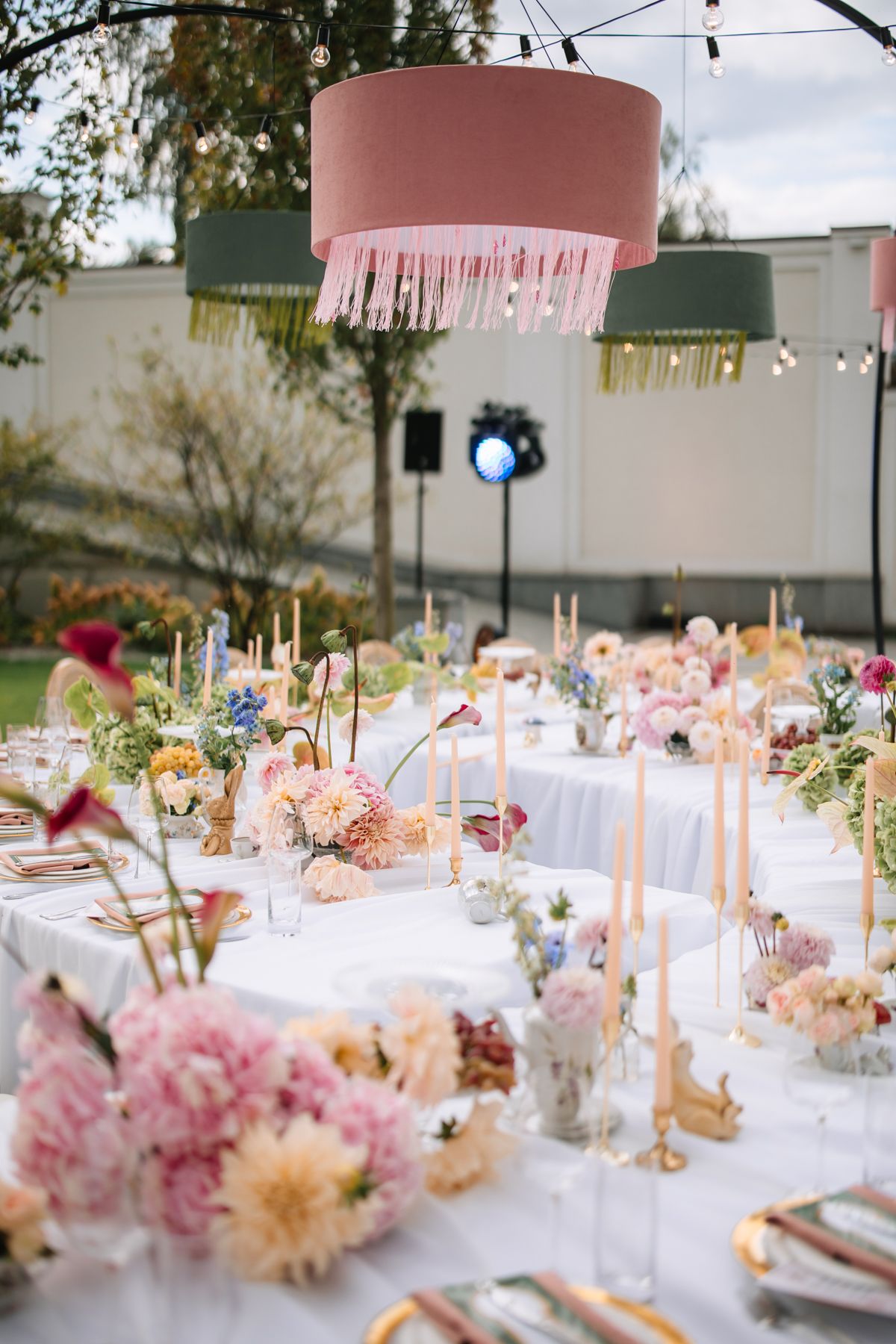 Elegant outdoor wedding reception tables decorated with pink floral arrangements and taper candles under string lights.