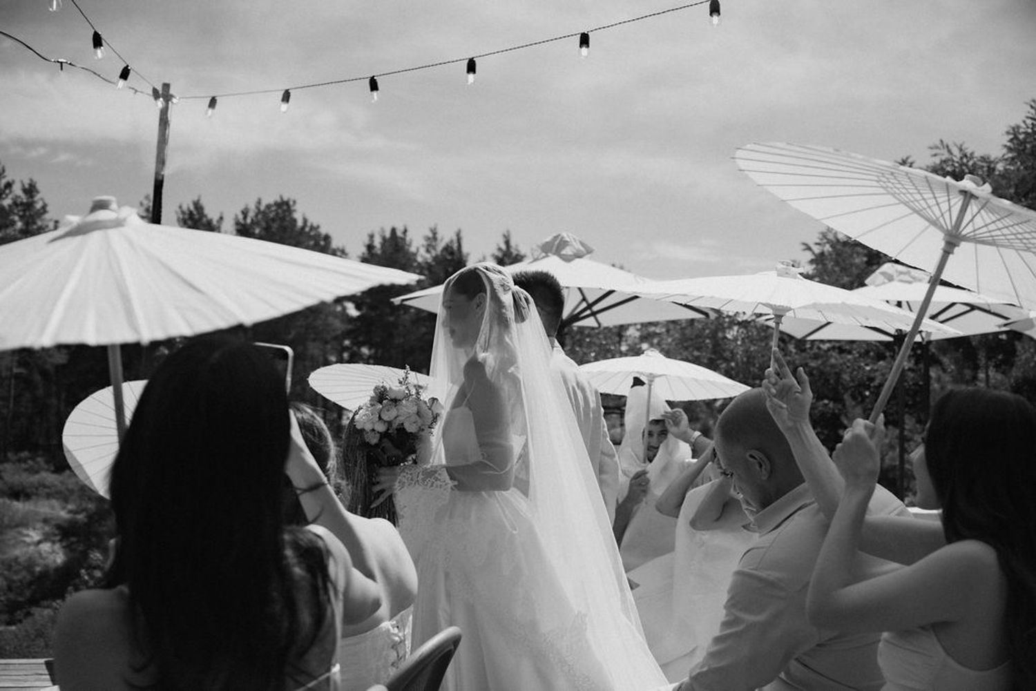 A series of black and white wedding photos showing string lights, umbrellas, and outdoor celebration moments.