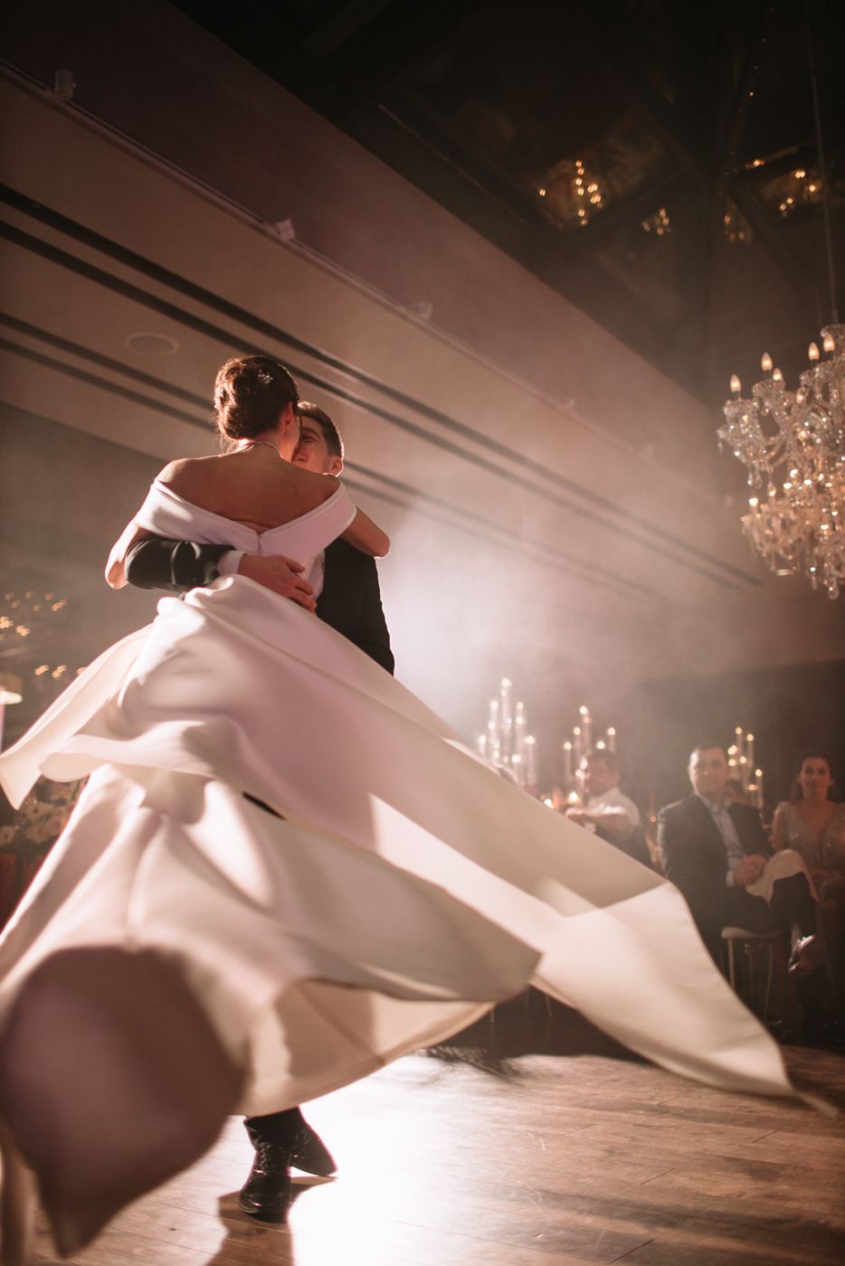 Couple dancing with flowing white dress under crystal chandeliers.