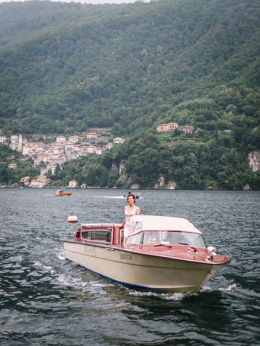 Classic wooden boat cruising on Lake Como with mountains and hillside villages in the background.