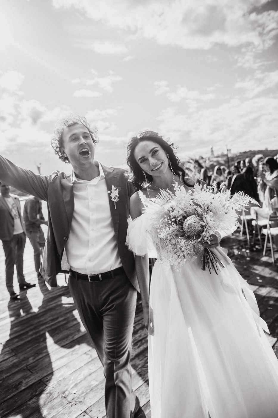 A joyful couple celebrates their outdoor wedding day while walking together in black and white.