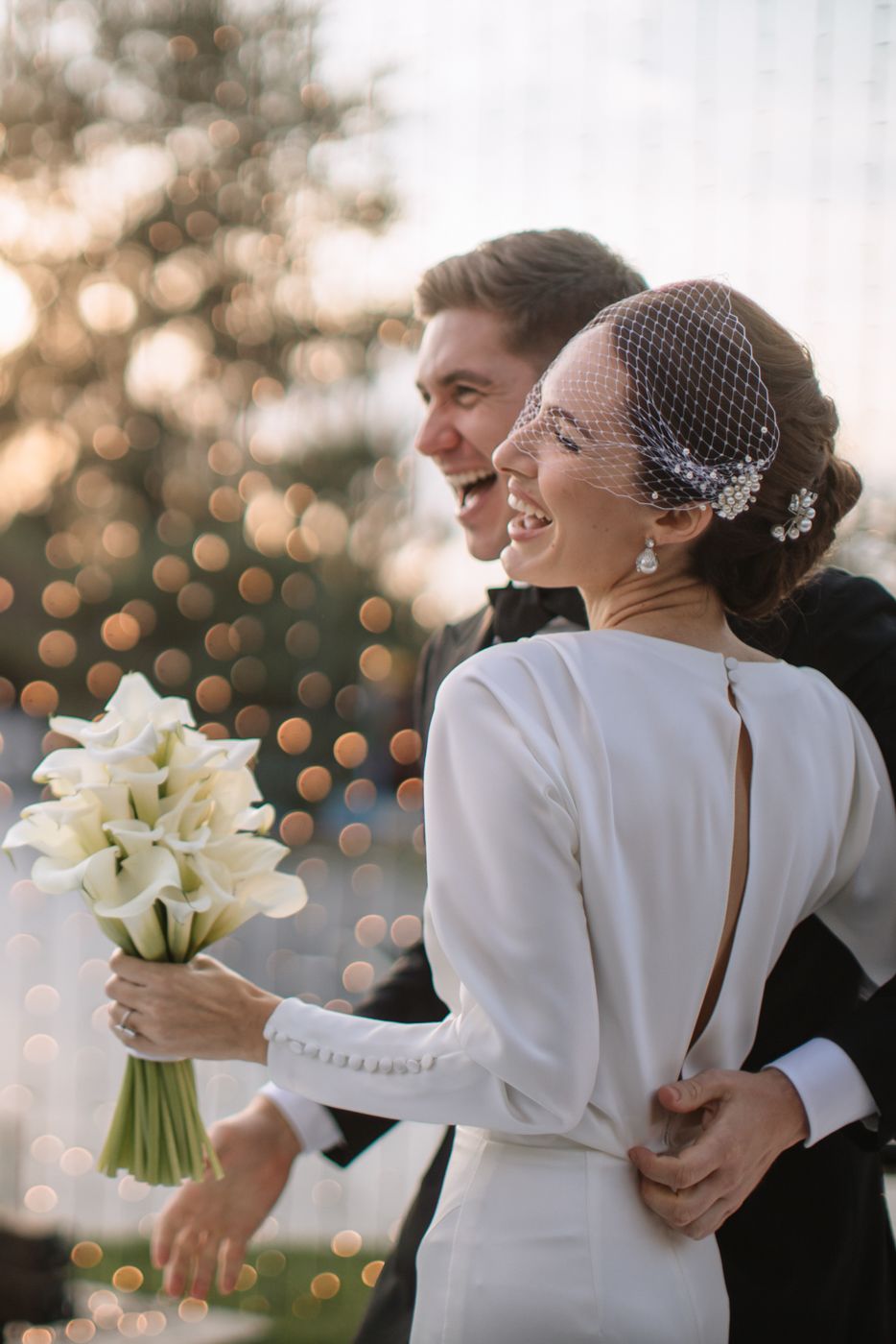 Romantic wedding couple embracing while holding a bouquet of white lilies.