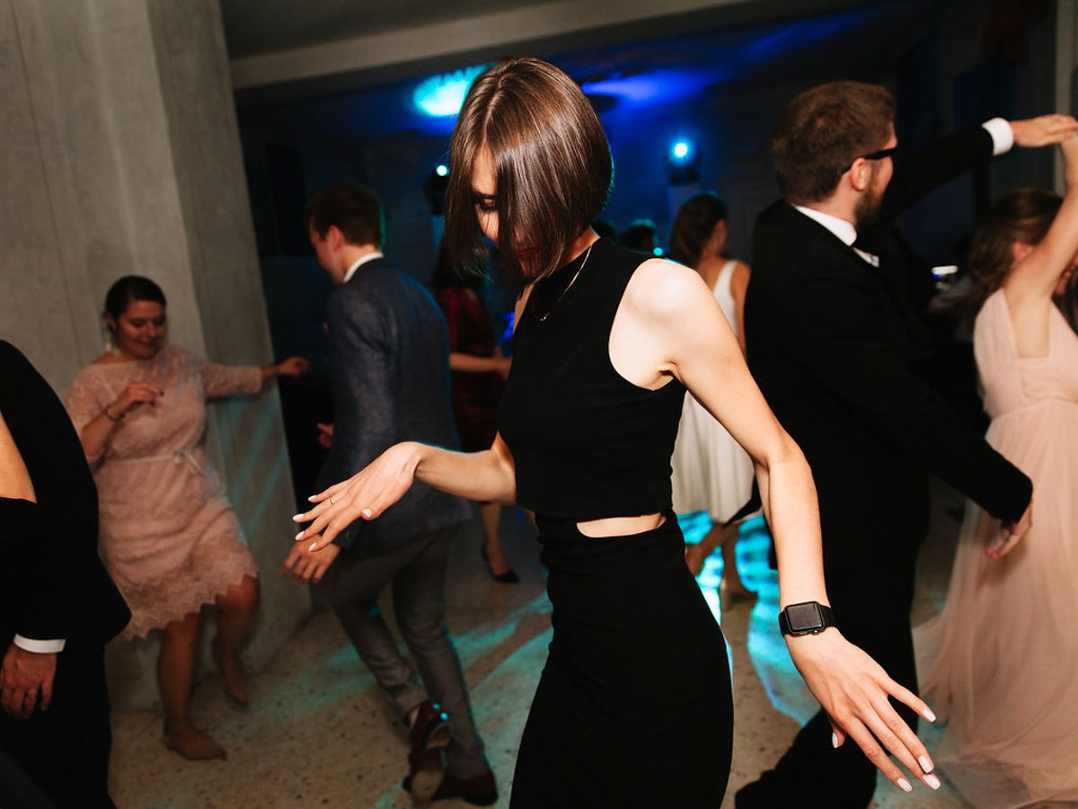 People dancing and socializing at a dimly lit party or nightclub with blue lighting in the background.
