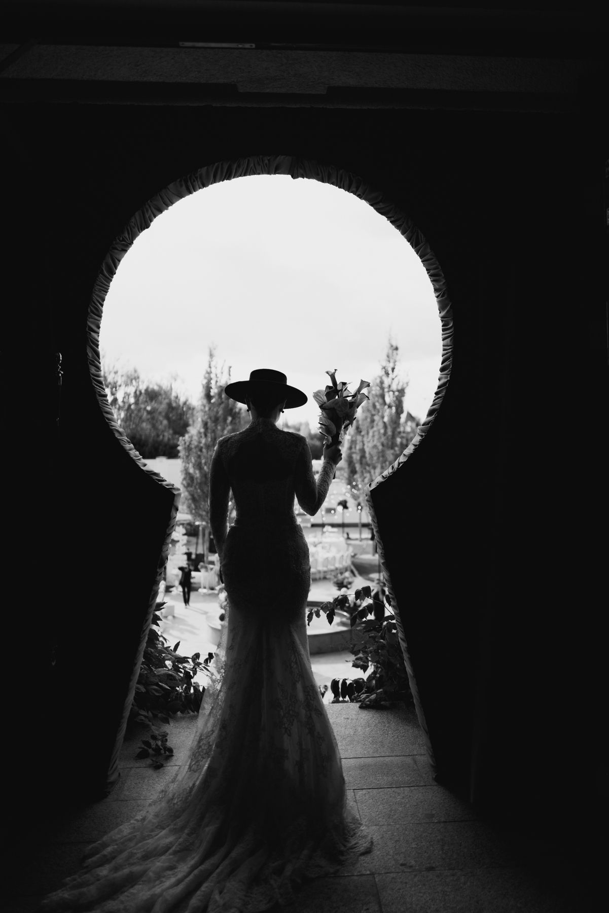 A silhouetted couple stands in a tunnel-like archway creating a dramatic backlit wedding photograph in black and white.