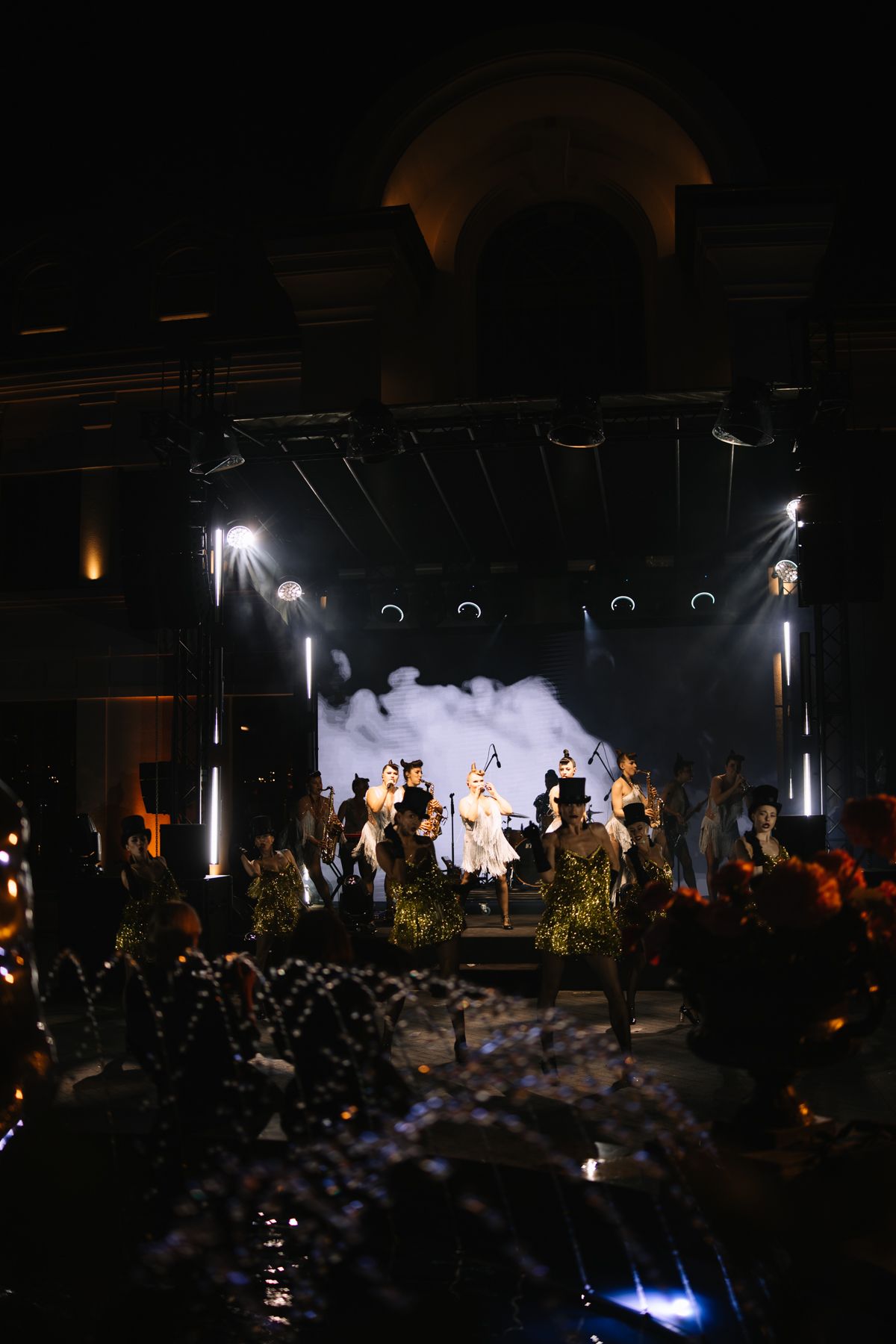 Dramatic concert performance with backlit performers on stage amid atmospheric fog and lighting effects.