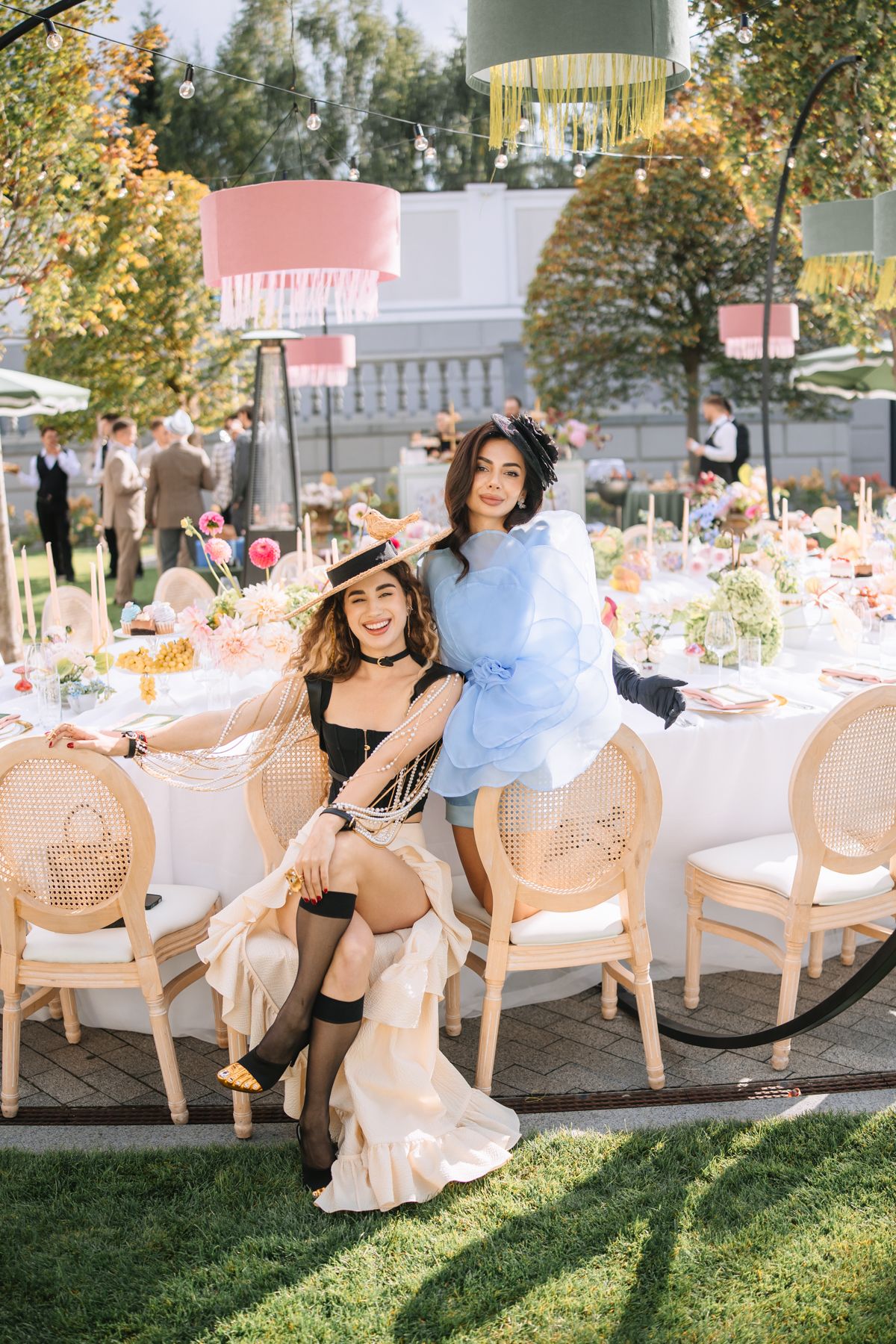 Elegant outdoor party setup with rattan chairs and white table settings on a sunny lawn.