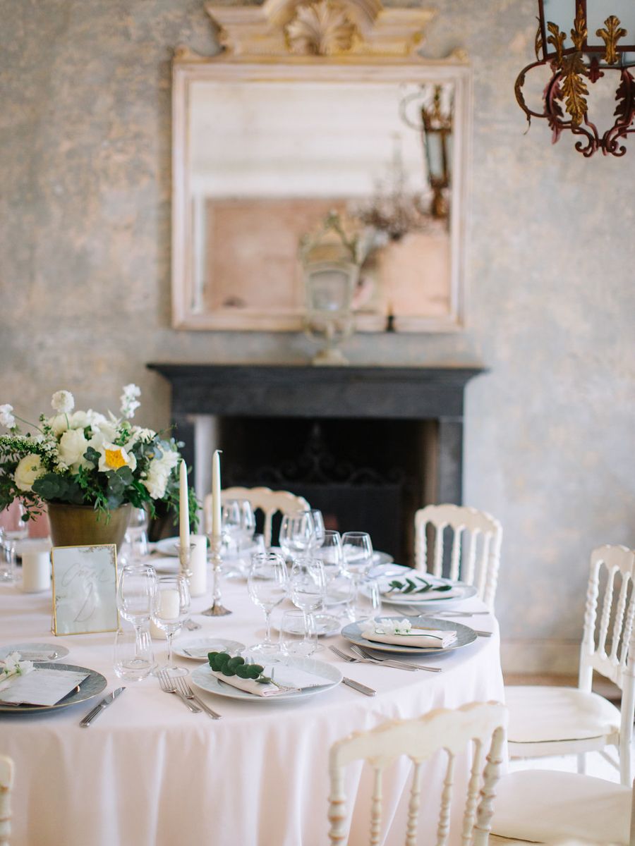 Elegant white table settings with crystal glassware in a rustic room with stone walls and vintage fireplace.